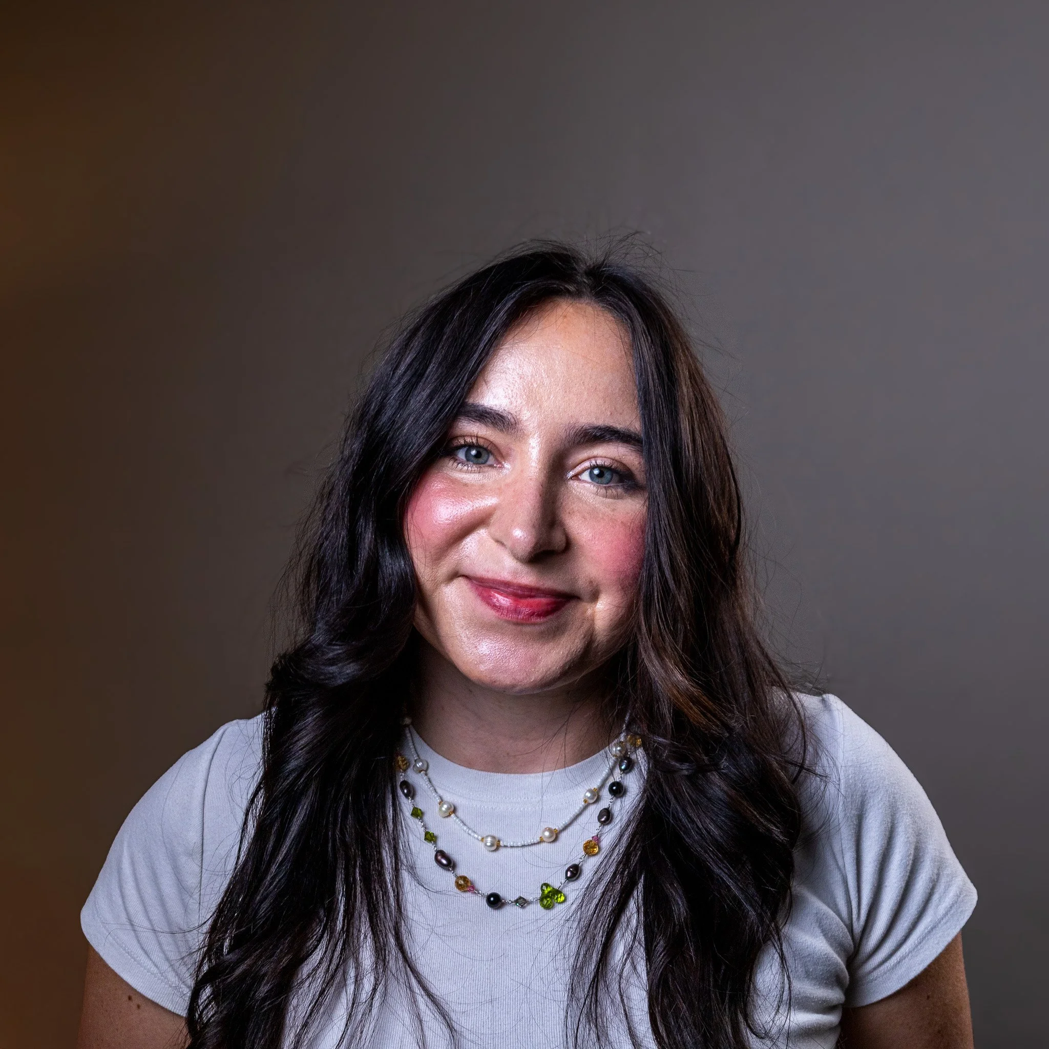 A woman with dark hair, wearing a black shirt, jeans, and jewelry, standing in front of a small airplane.