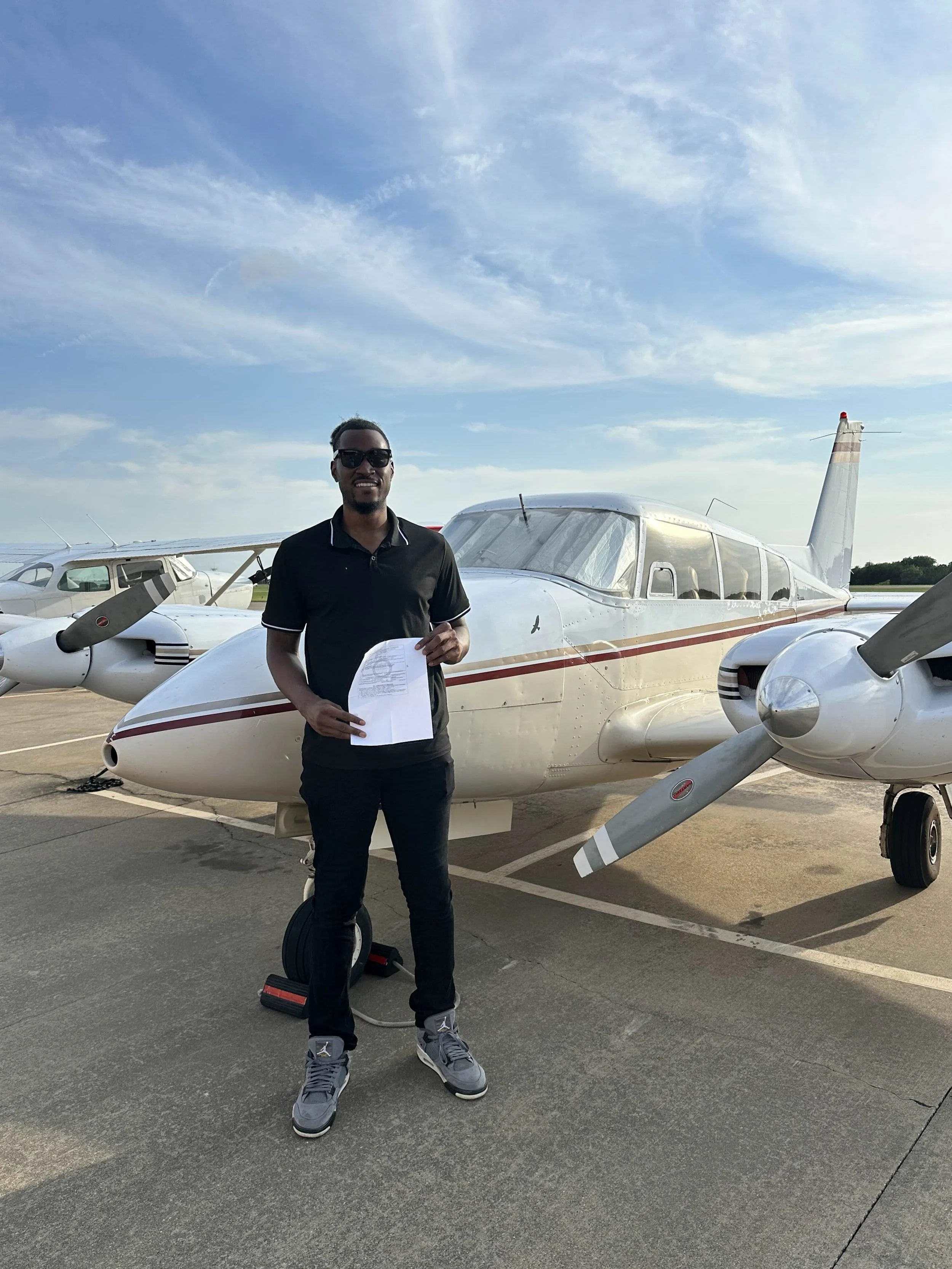 A man standing in front of a small white airplane holding a paper, with a clear sky in the background.
