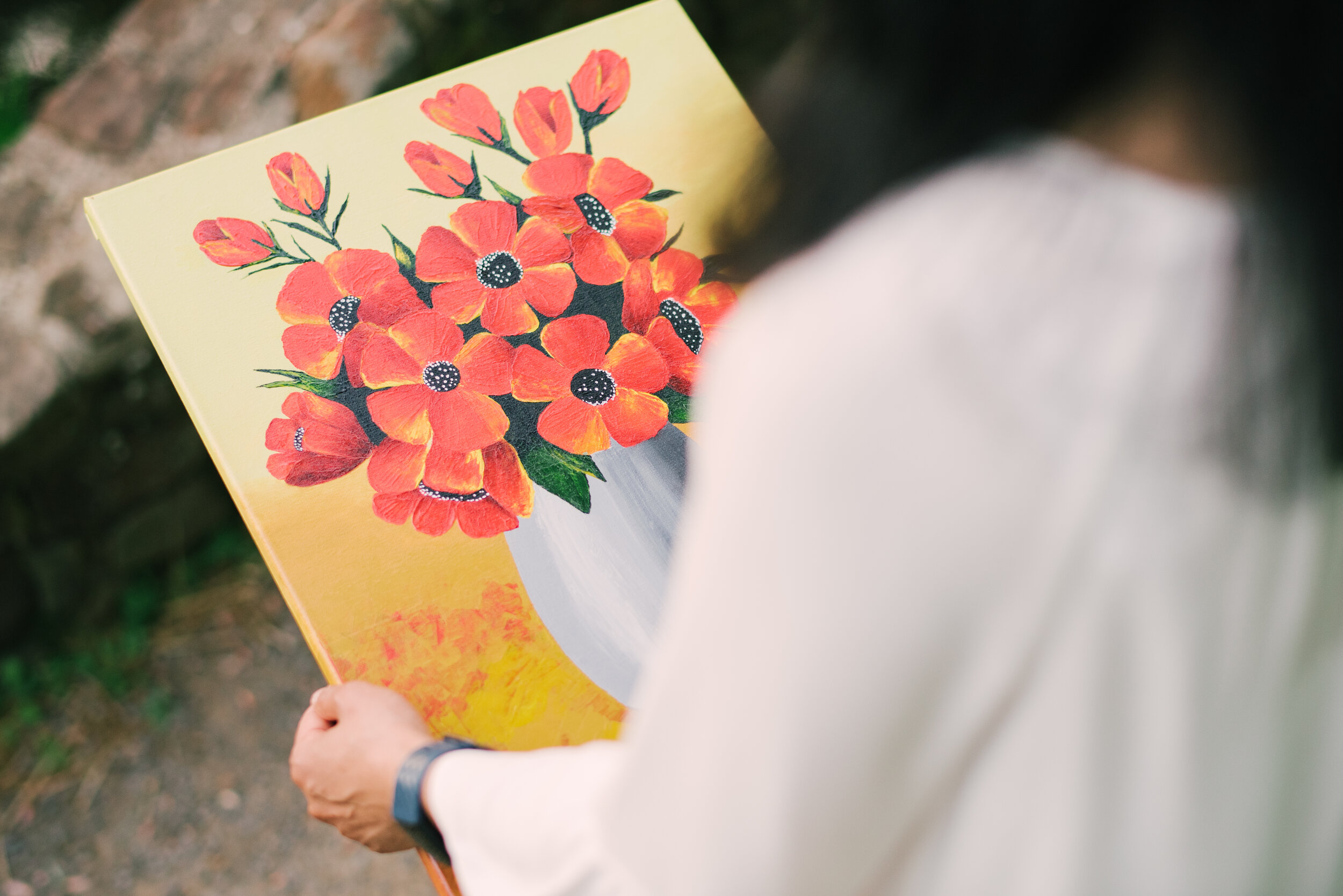 Person holding a painting of red flowers in a white vase