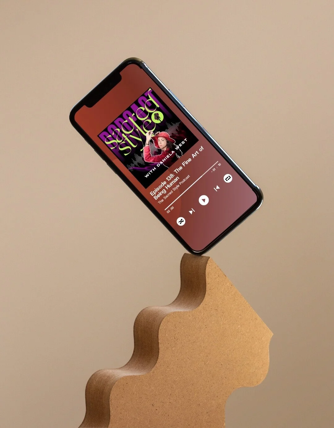A smartphone displaying a podcast episode titled "Episode 138: The Fine Art of Being Human" on a beige wavy stand against a beige background.