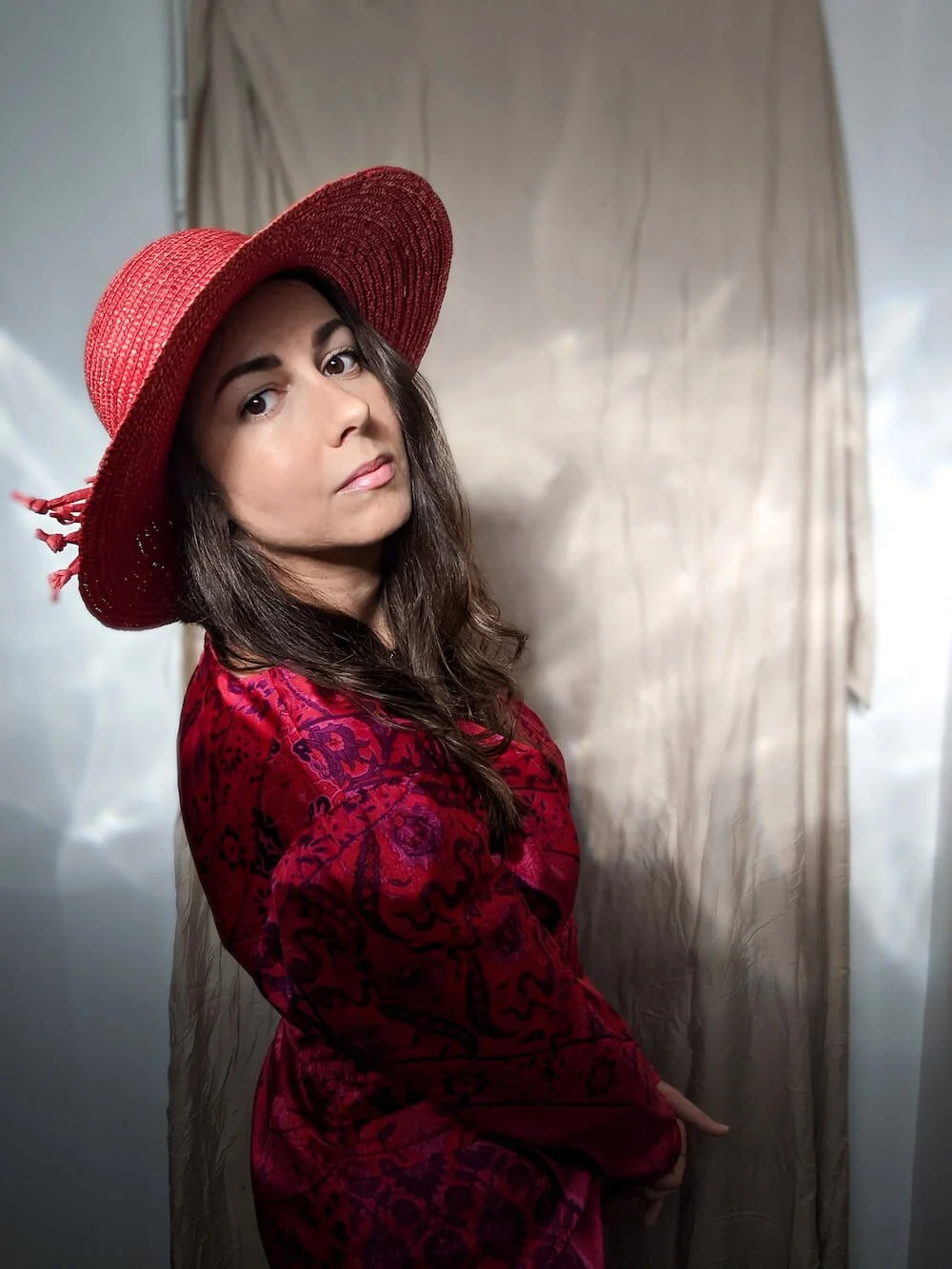A woman wearing a red sunhat and a red dress with black patterns, standing in front of a beige backdrop.