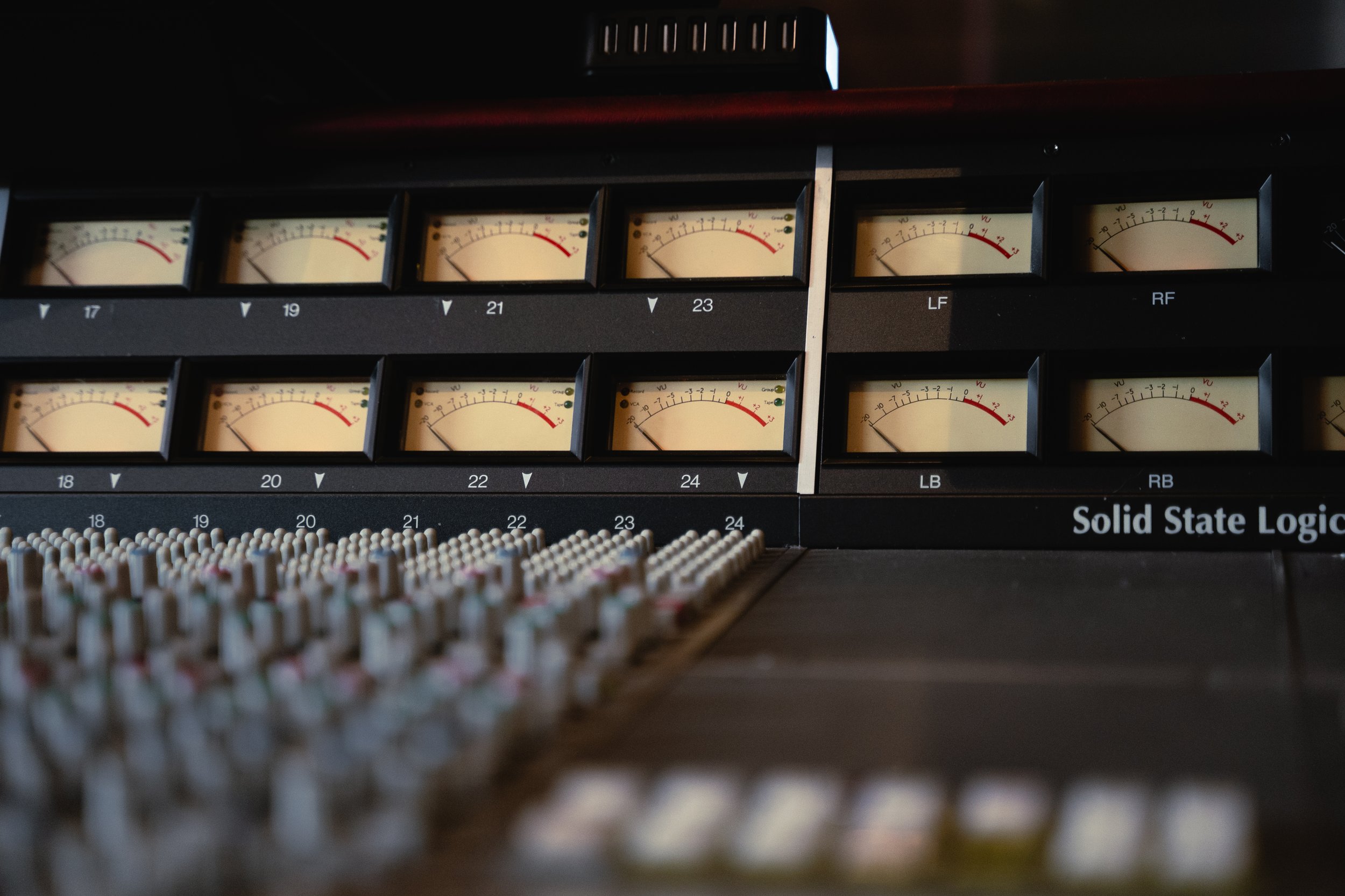 Audio mixing console with multiple analog level meters and control knobs, labeled 'Solid State Logic'.