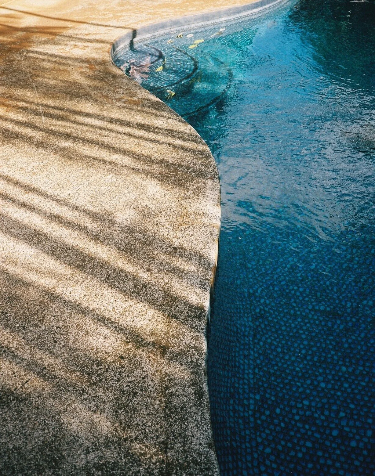 Close-up of a swimming pool's edge with textured concrete deck and blue water.