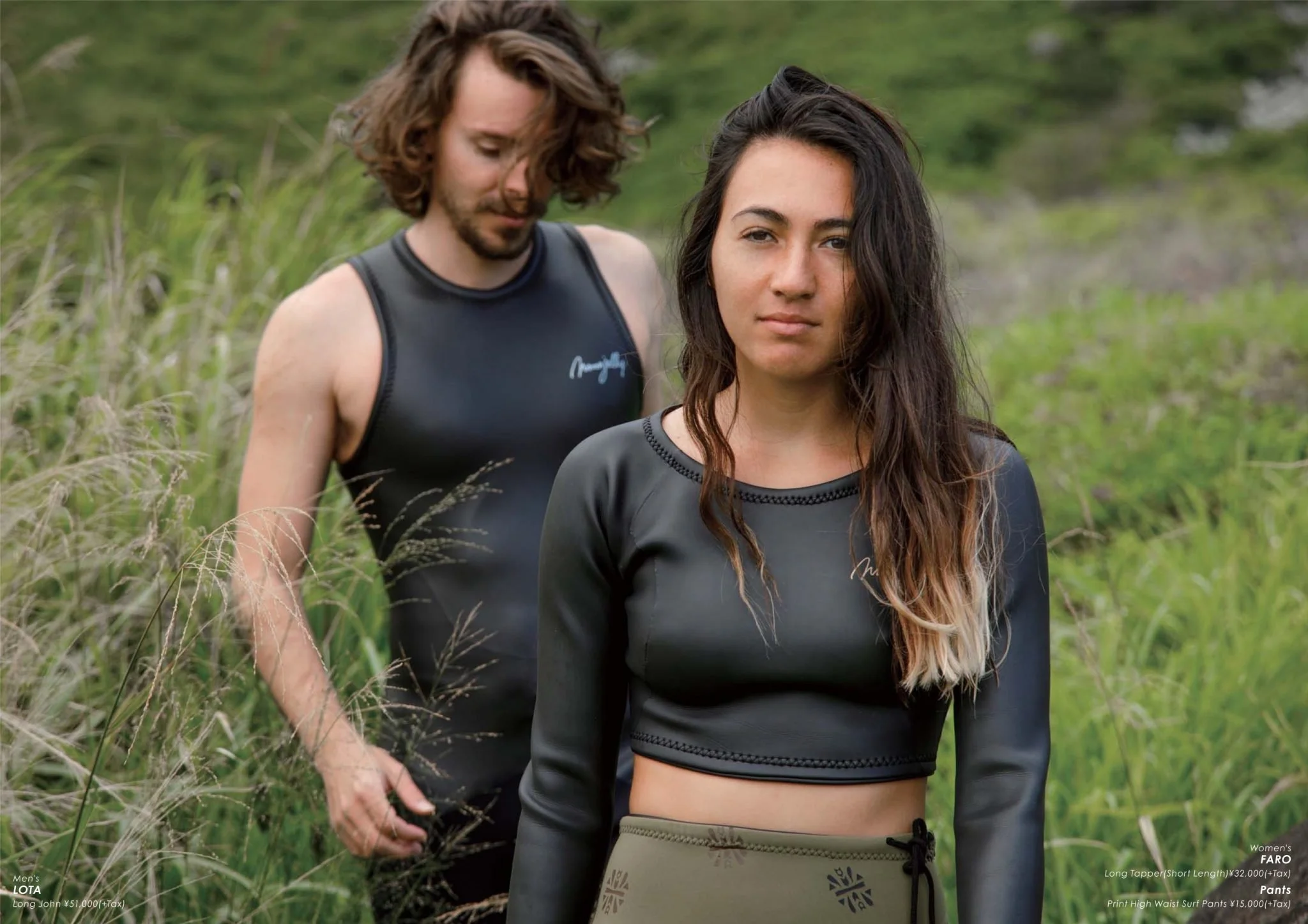 A man with wavy brown hair and a woman with long, wavy dark hair with blonde tips standing outdoors in tall grass, both wearing black athletic tops.