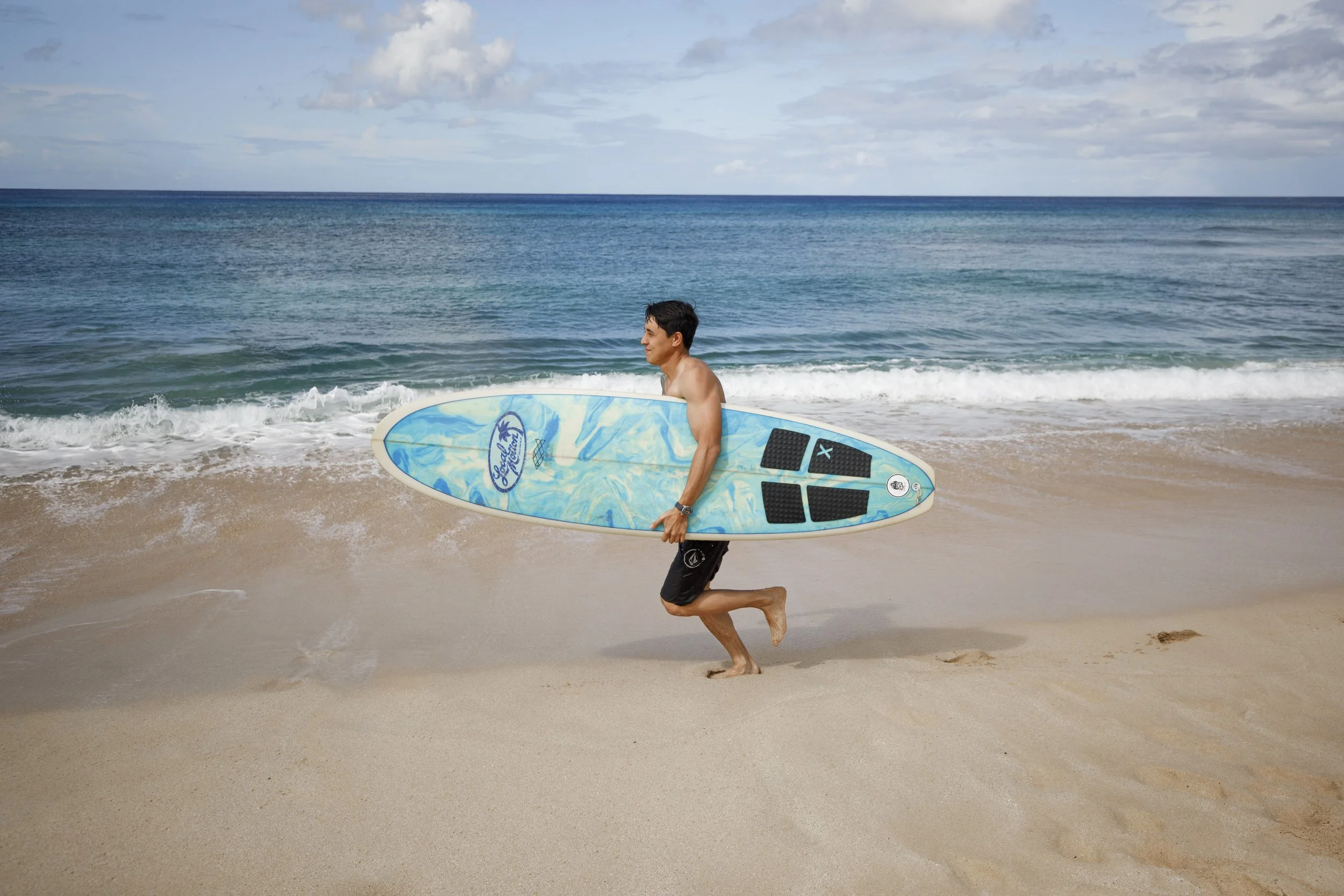 A man carrying a surfboard walking on the sandy beach near the ocean waves.