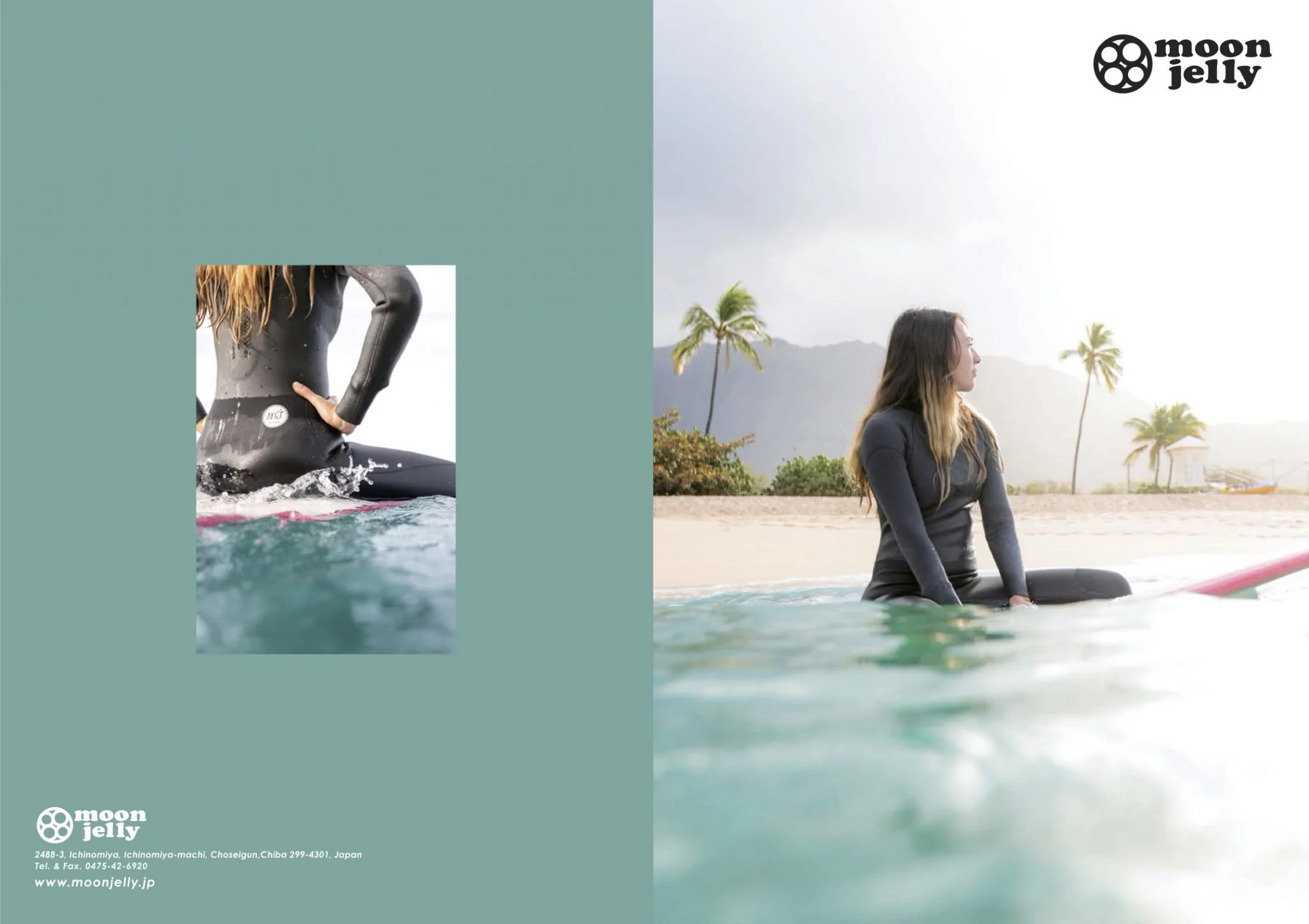 A woman sitting on a surfboard in the water at the beach, with palm trees and mountains in the background, wearing a wetsuit.