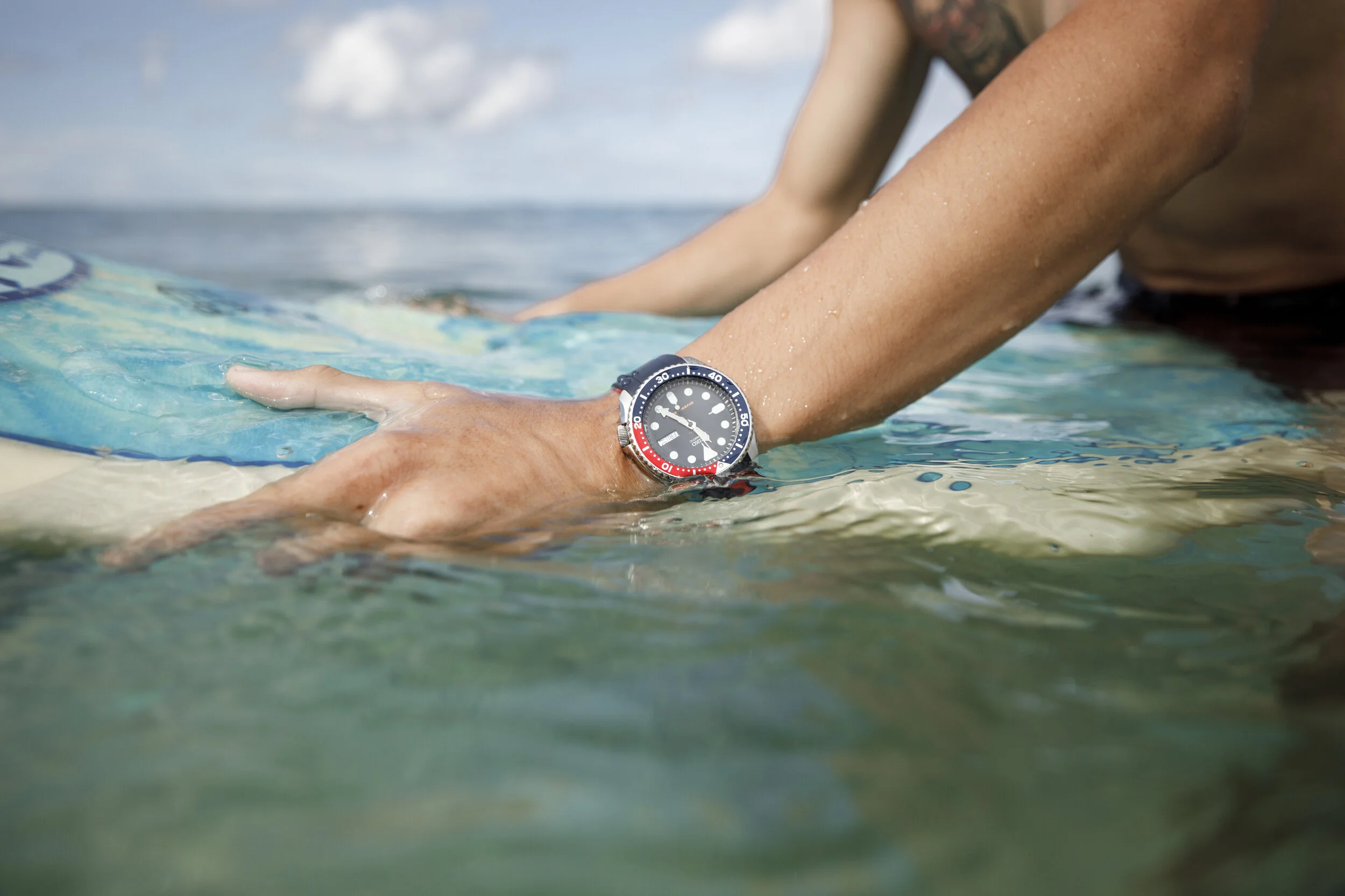 A person wearing a Seiko diver's watch paddling on a surfboard in the ocean.