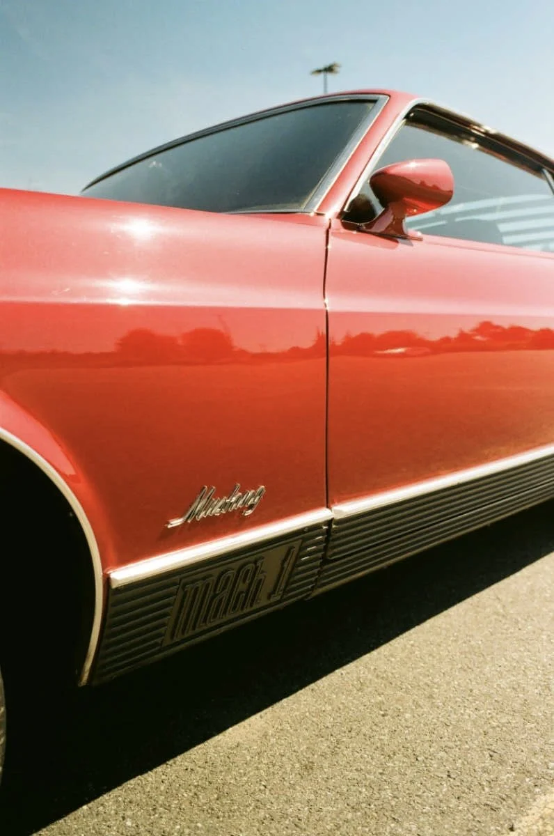 Red Ford Mustang parked outdoors on a sunny day, showing the side view with a focus on the door and side mirror.