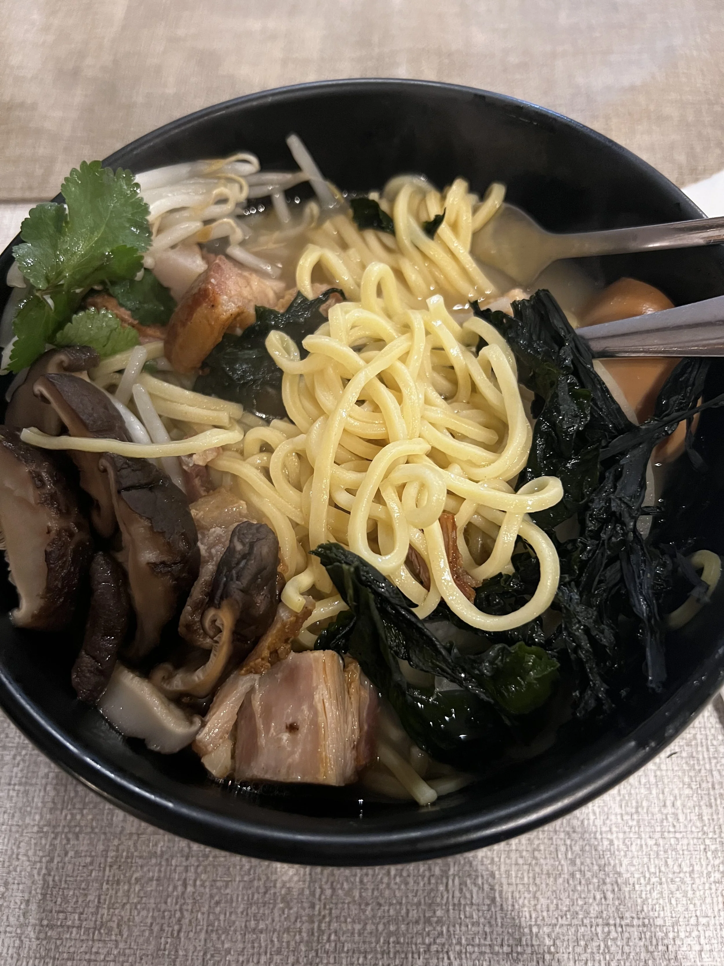 Bowl of ramen noodles with mushrooms, pork, seaweed, bean sprouts, cilantro, and broth.