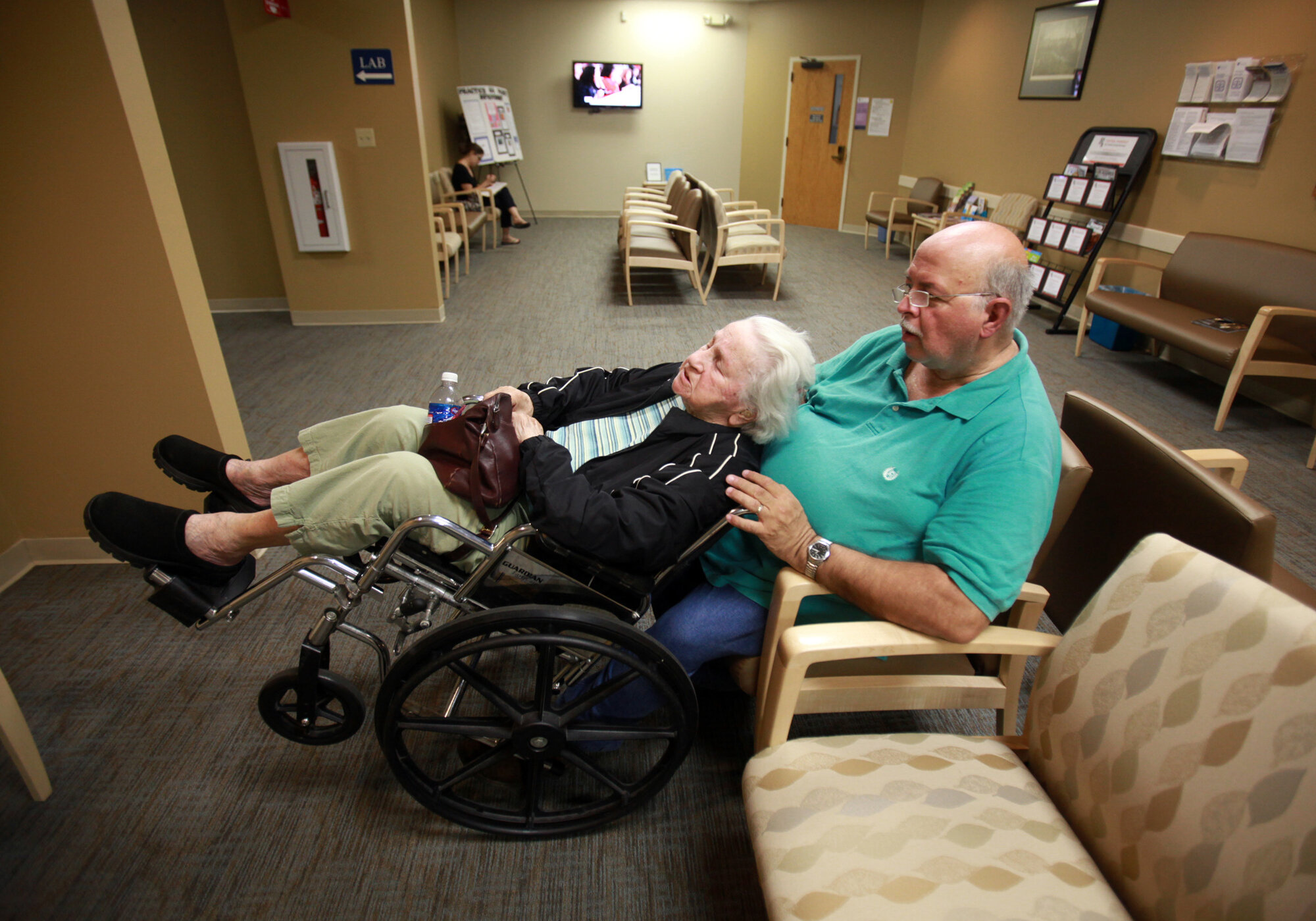  Danny tips Elizabeth's wheelchair against his chest to help alleviate pain in her neck while waiting at the doctor's office.  Elizabeth has a hard time sitting up for long periods of time and requested to go home after spending 20 minutes in the wai