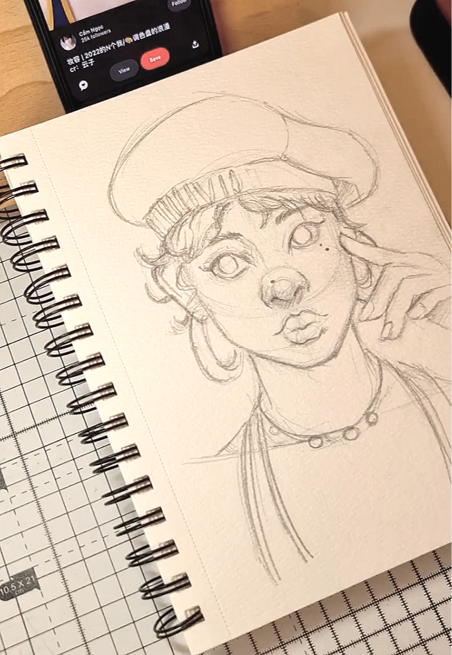 A pencil sketch of a young woman wearing a beret, with short, wavy hair, large expressive eyes, and a small beauty mark near her eye. She is touching her face with one hand and wearing a necklace, with a casual and thoughtful expression.