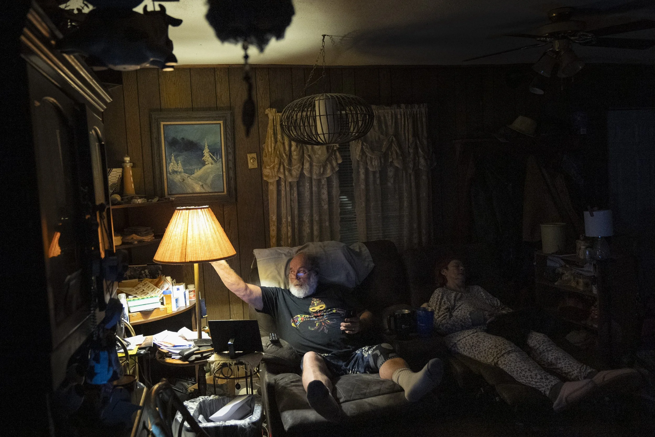  With Lynne already sound asleep, Wayne reaches up to turn out the light for the night after arriving home from his newspaper delivery route. They started spending the night in their two recliners, which accommodated Lynne’s limited mobility. Wayne c