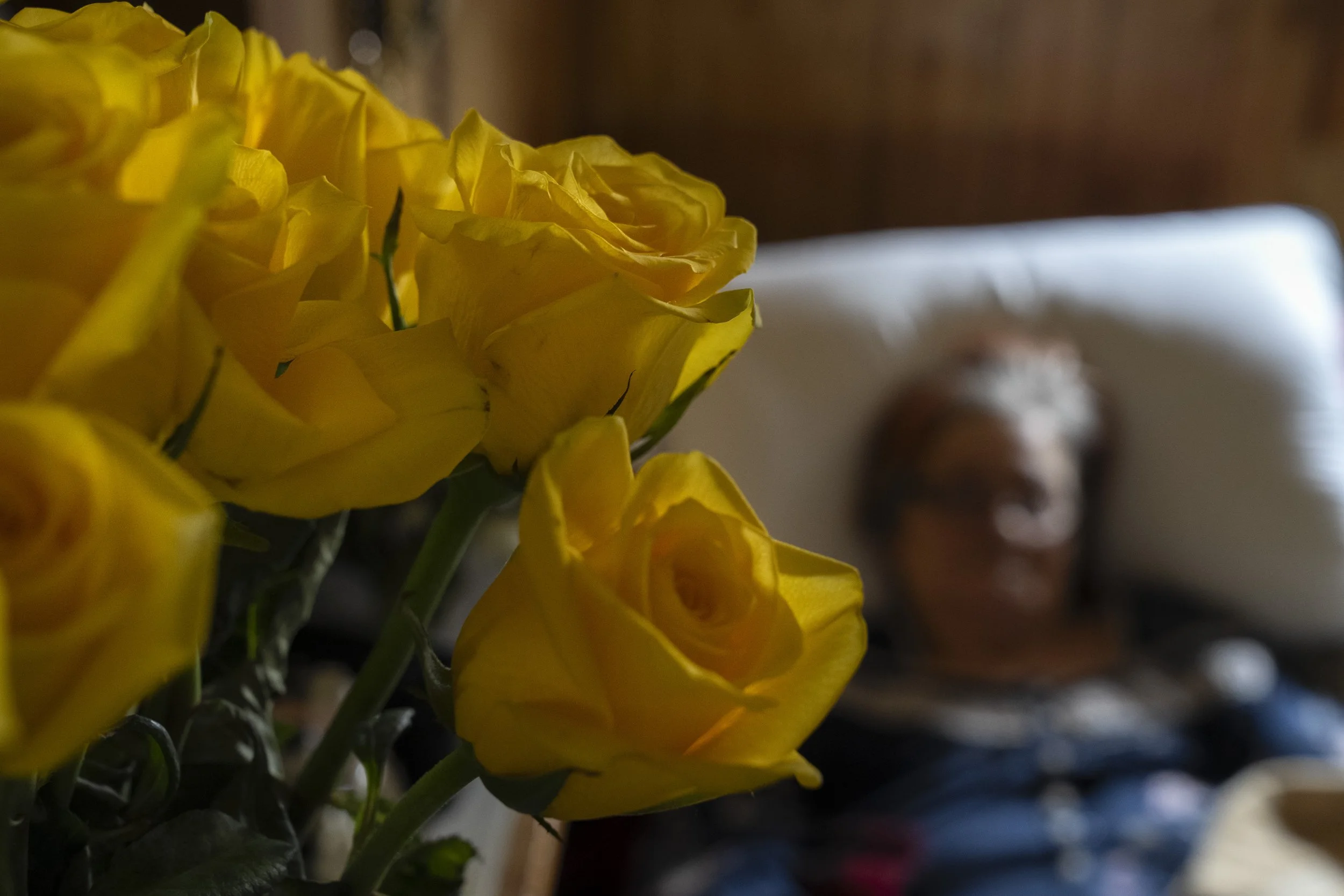  Yellow roses from Wayne rest in a vase above where Lynne sleeps in a hospital bed. As her cognitive function declined, Wayne noted that she seemed to find more comfort in having her favorite-colored flowers nearby. “She was one of the toughest women