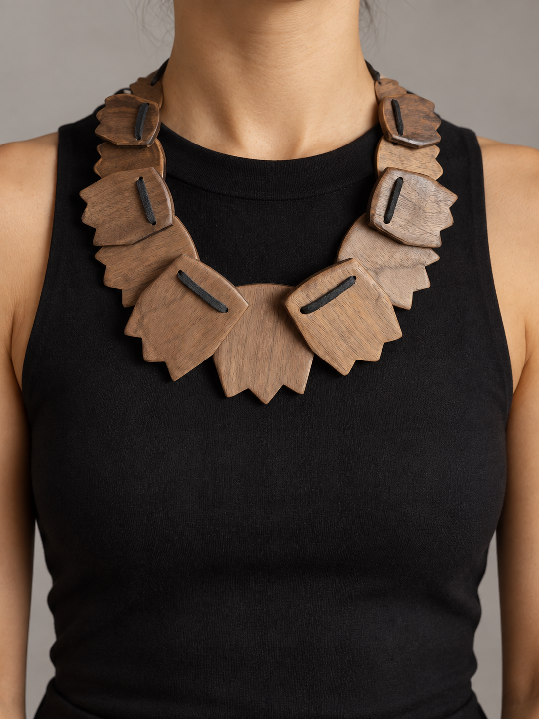 Woman wearing a black sleeveless top and a large statement necklace made of carved wooden pieces.