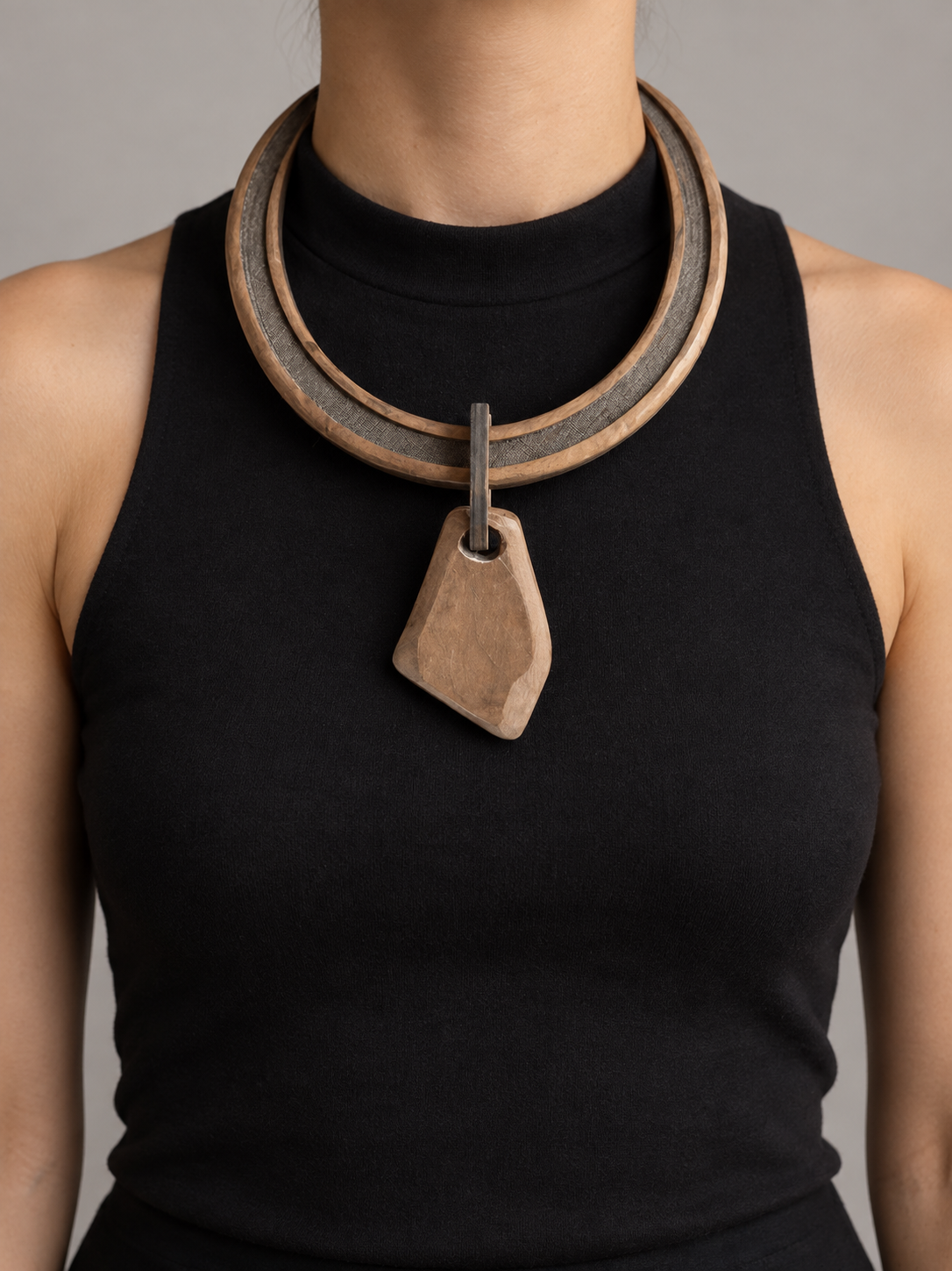 A woman wearing a statement necklace with multiple concentric wooden and metal rings and a large geometric wooden pendant on a black sleeveless top.