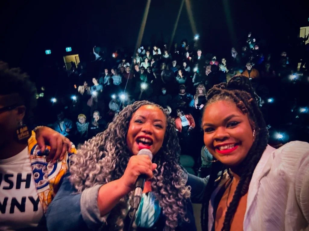 Performer selfies with audience in the background.