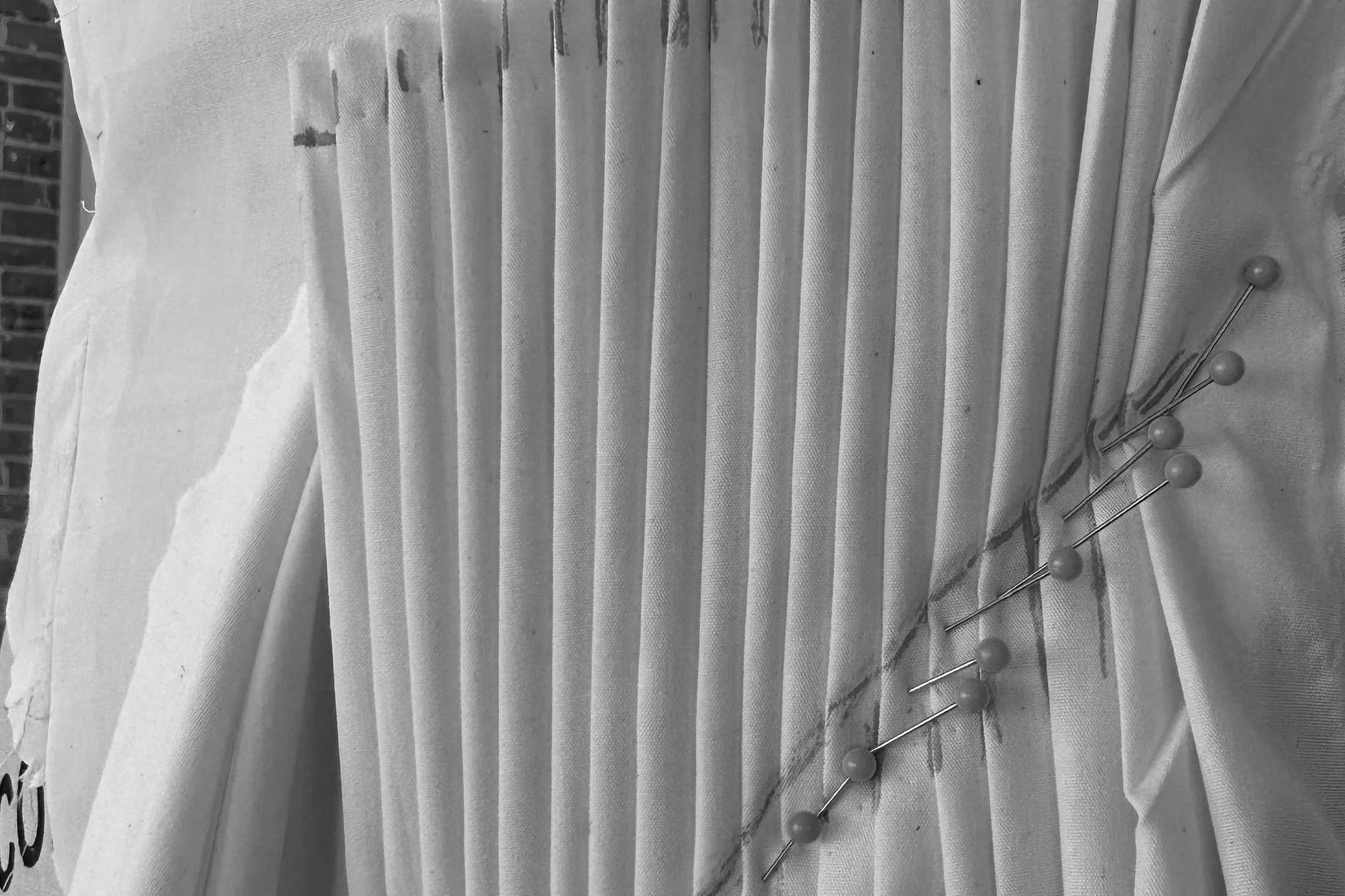 Close-up of pleated fabric held with yellow-headed sewing pins and blue markings.