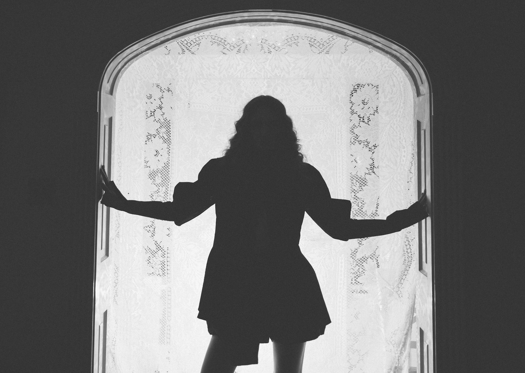 Silhouette of a person standing in front of a lace-covered window.