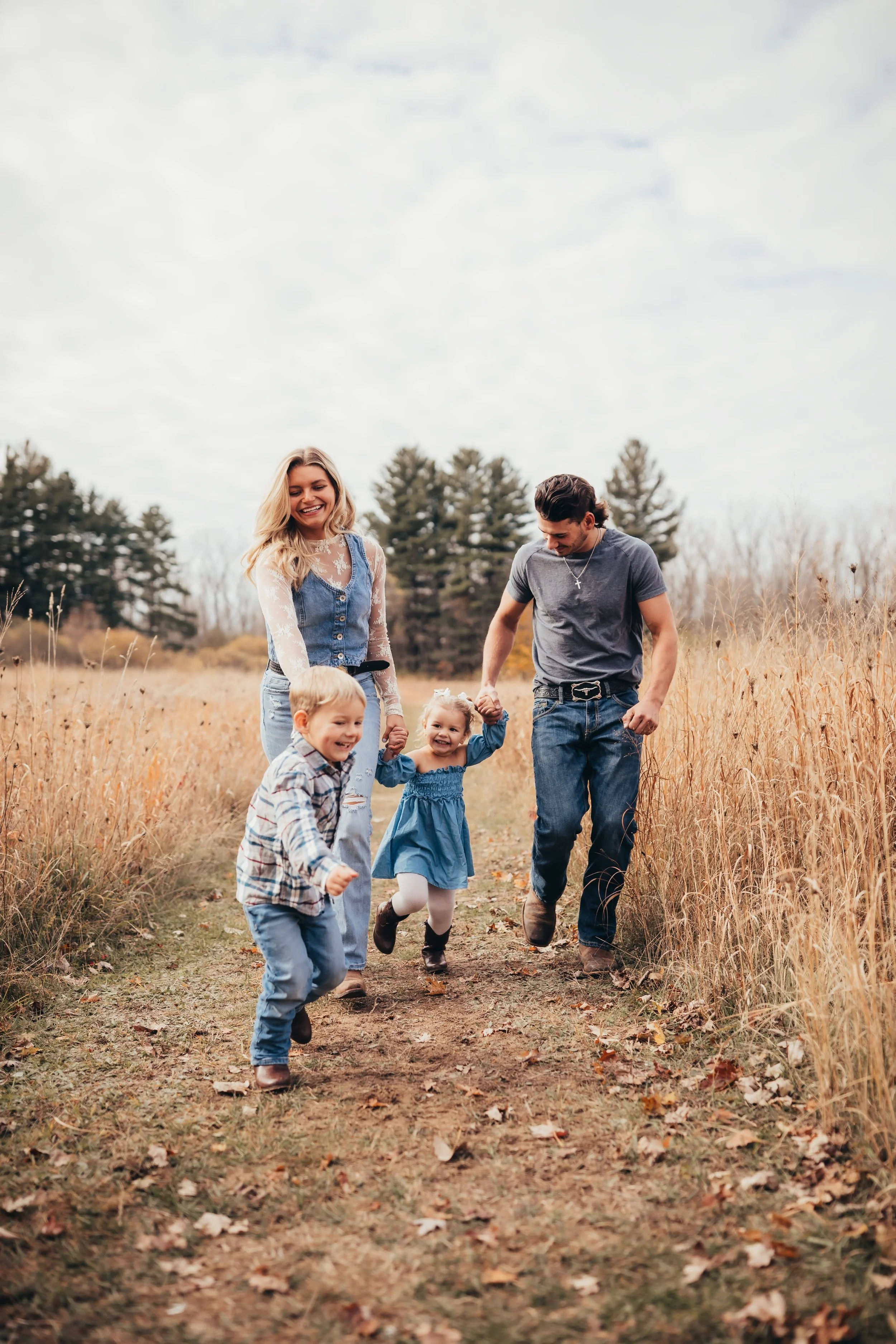 Lifestyle family photography session with parents and young children walking and laughing through a grassy field