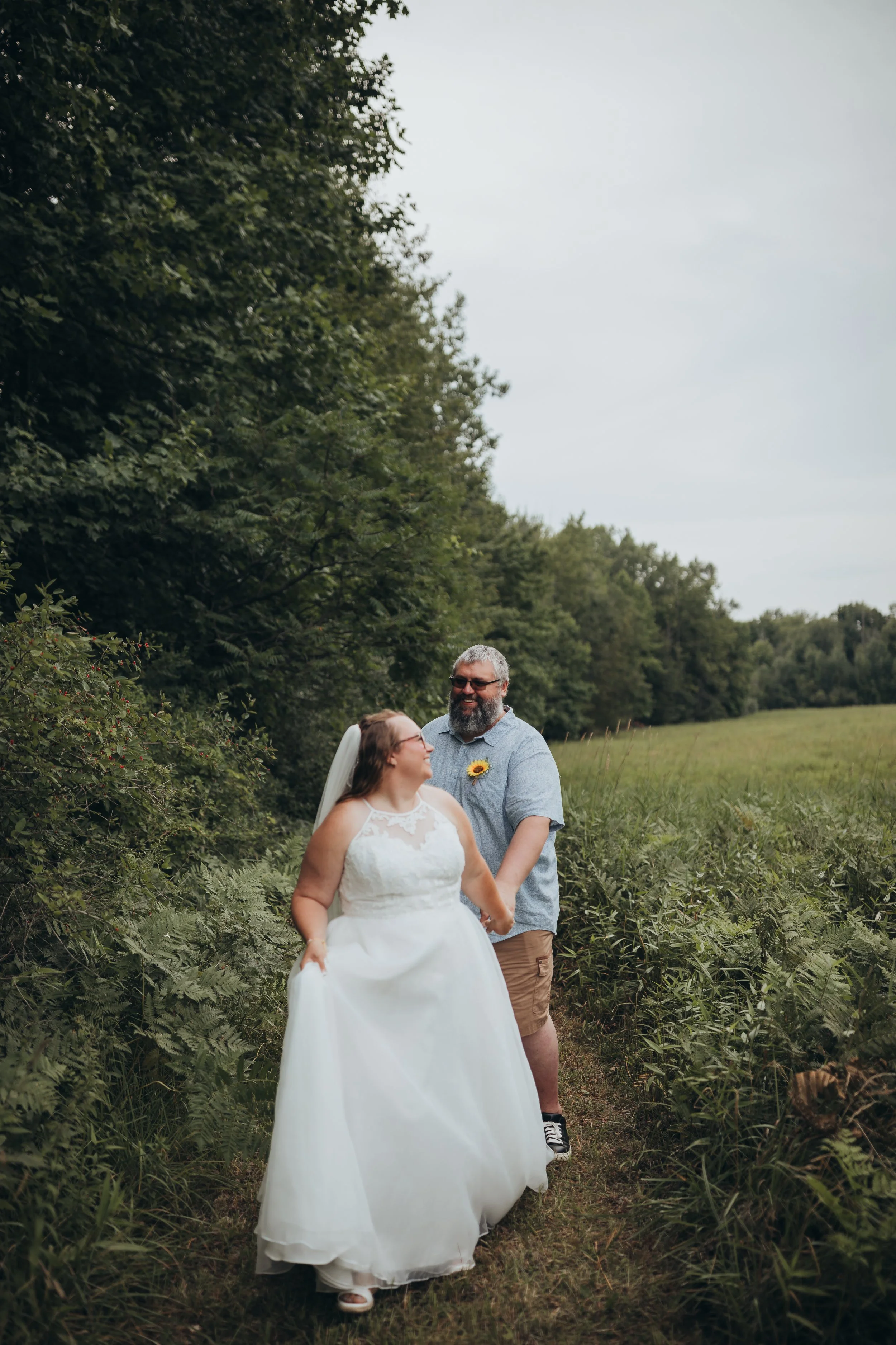Moody, candid wedding portrait of bride and groom walking through a field.