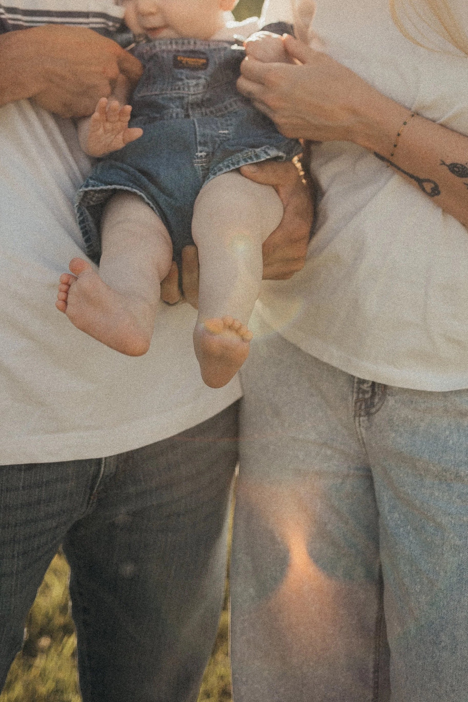 Cinematic photo of mom and dad holding their baby between them without faces showing.