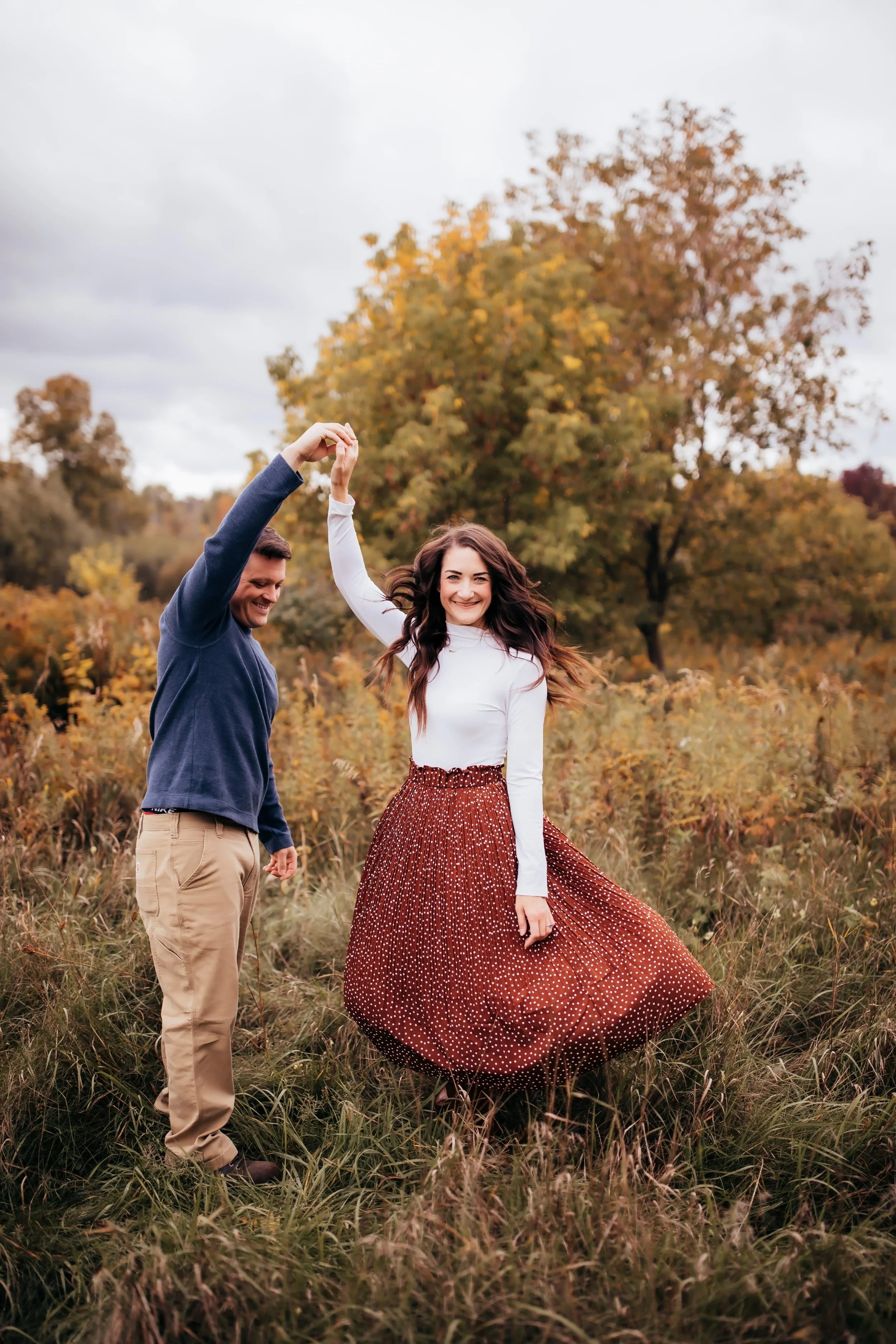 Couples photo session dancing together in a grassy field during fall with warm autumn colors at Black Creek Park