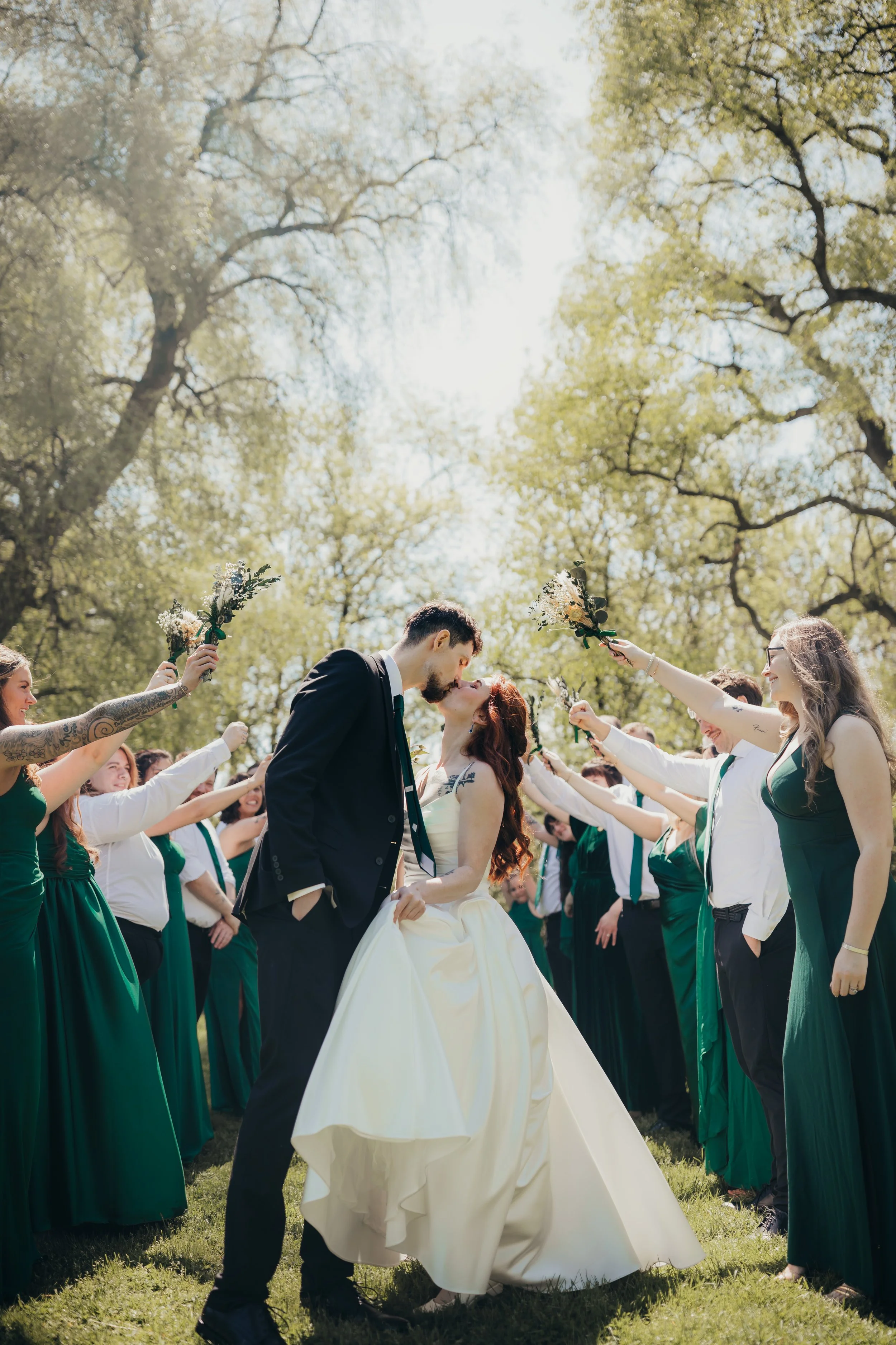 Outdoor candid wedding portrait of bride and groom sharing a kiss after they ran through bridal party tunnel