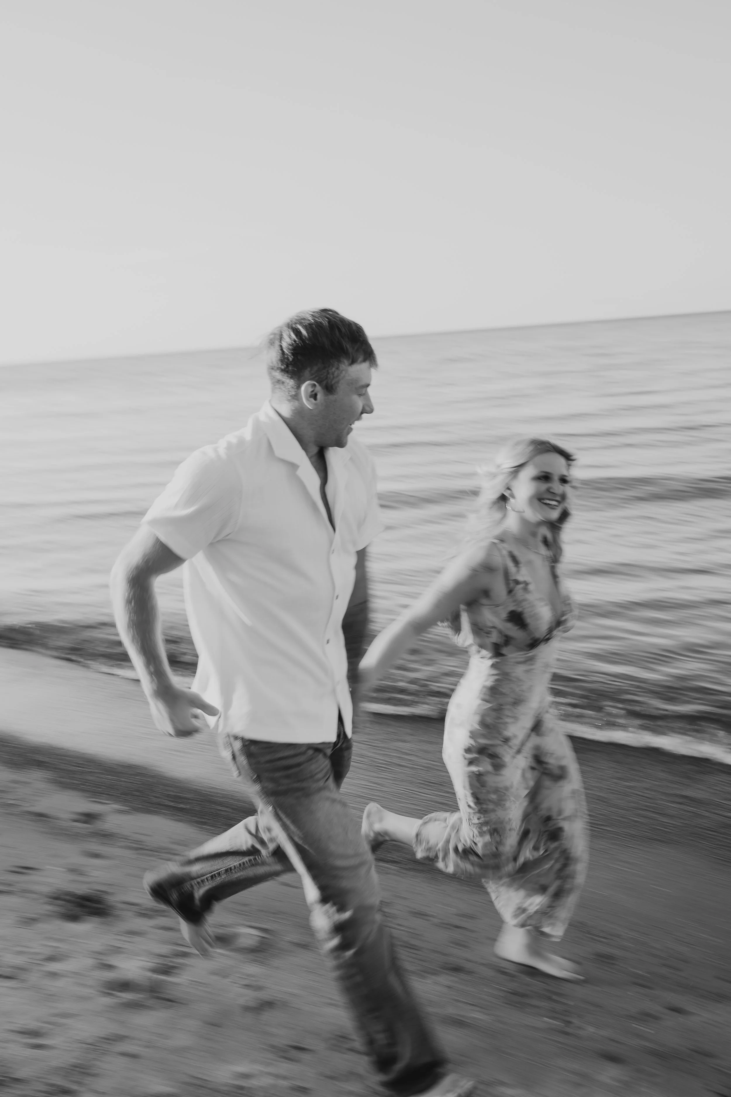 Black and white motion blur photo of a couple running down the beach together during sunset.