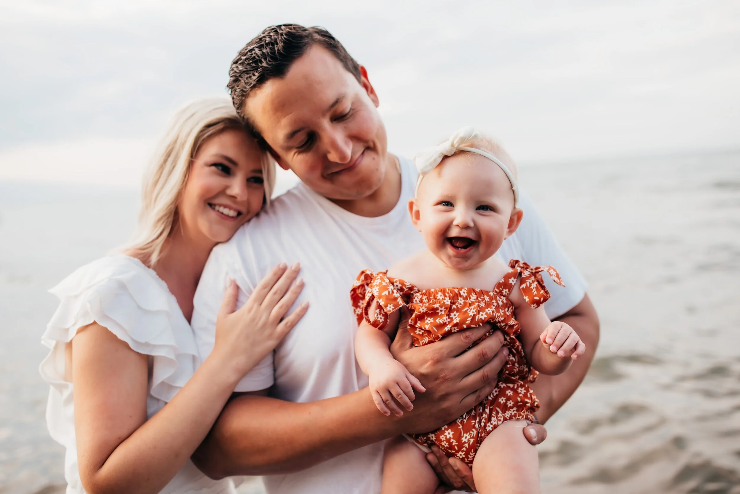 Candid family portrait of parents holding their smiling baby during golden hour