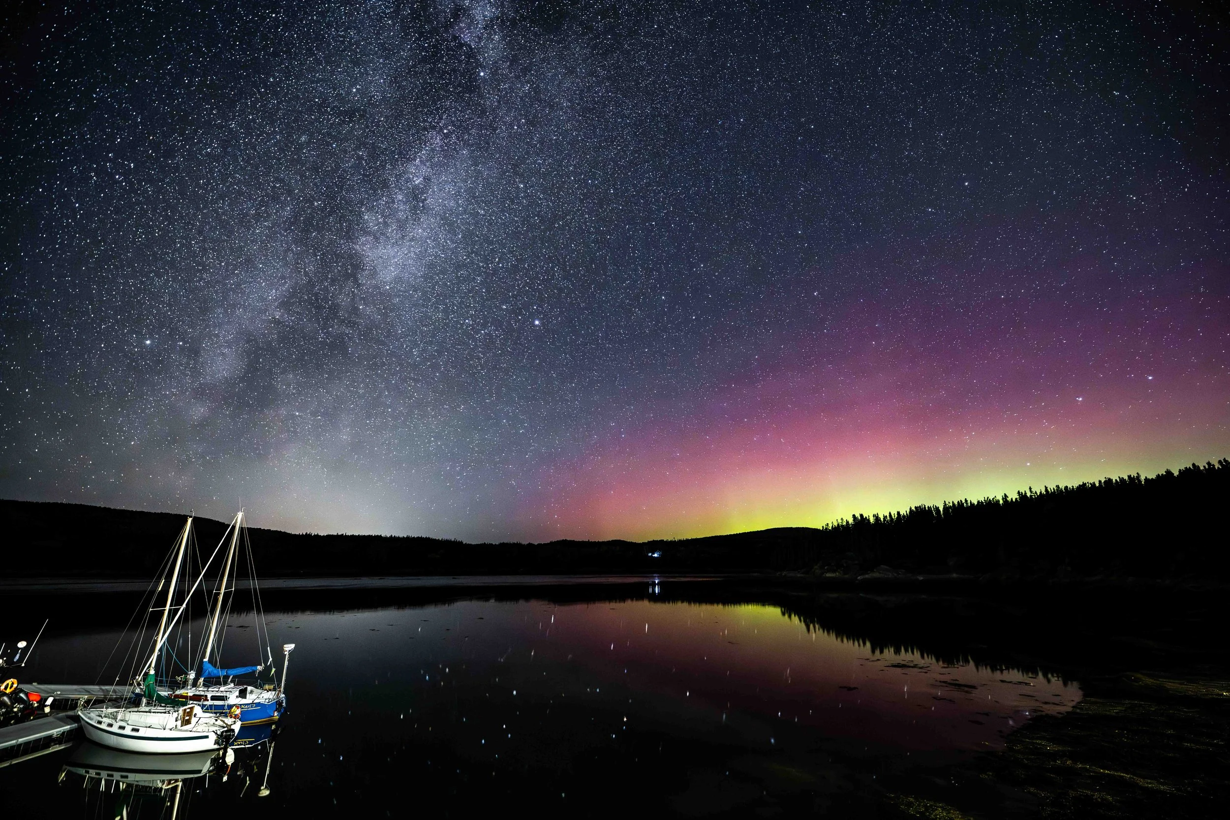 aurores boréales et voie lactée au quai de bergeronnes sur la cote-nord du quebec avec les bateaux en premier plan