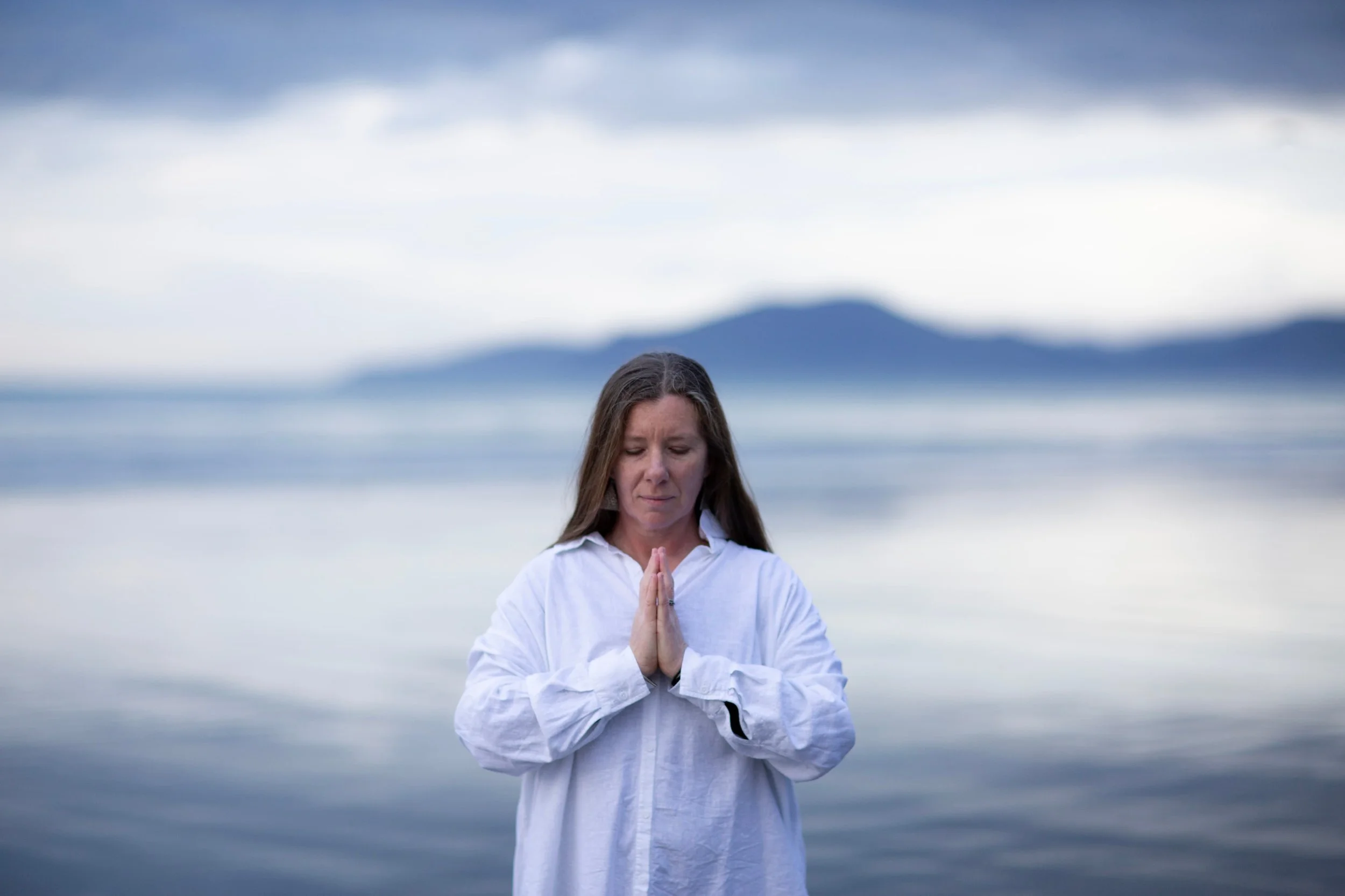 Yoga therapist Hayley by the ocean with hands in prayer, embodying presence and calm