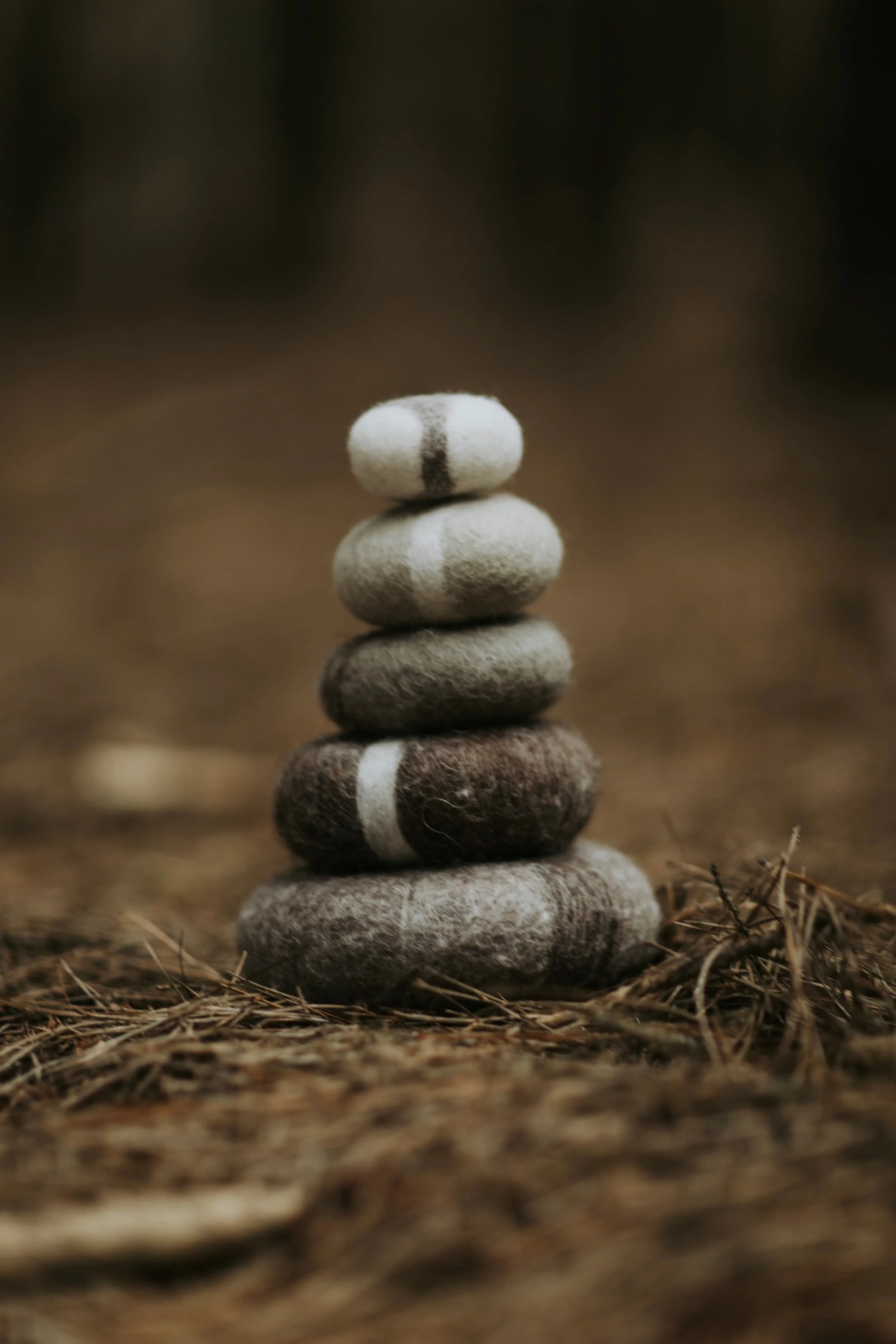 Handmade wool stones arranged as cairns in the forest, symbolising care, balance, and gentle support