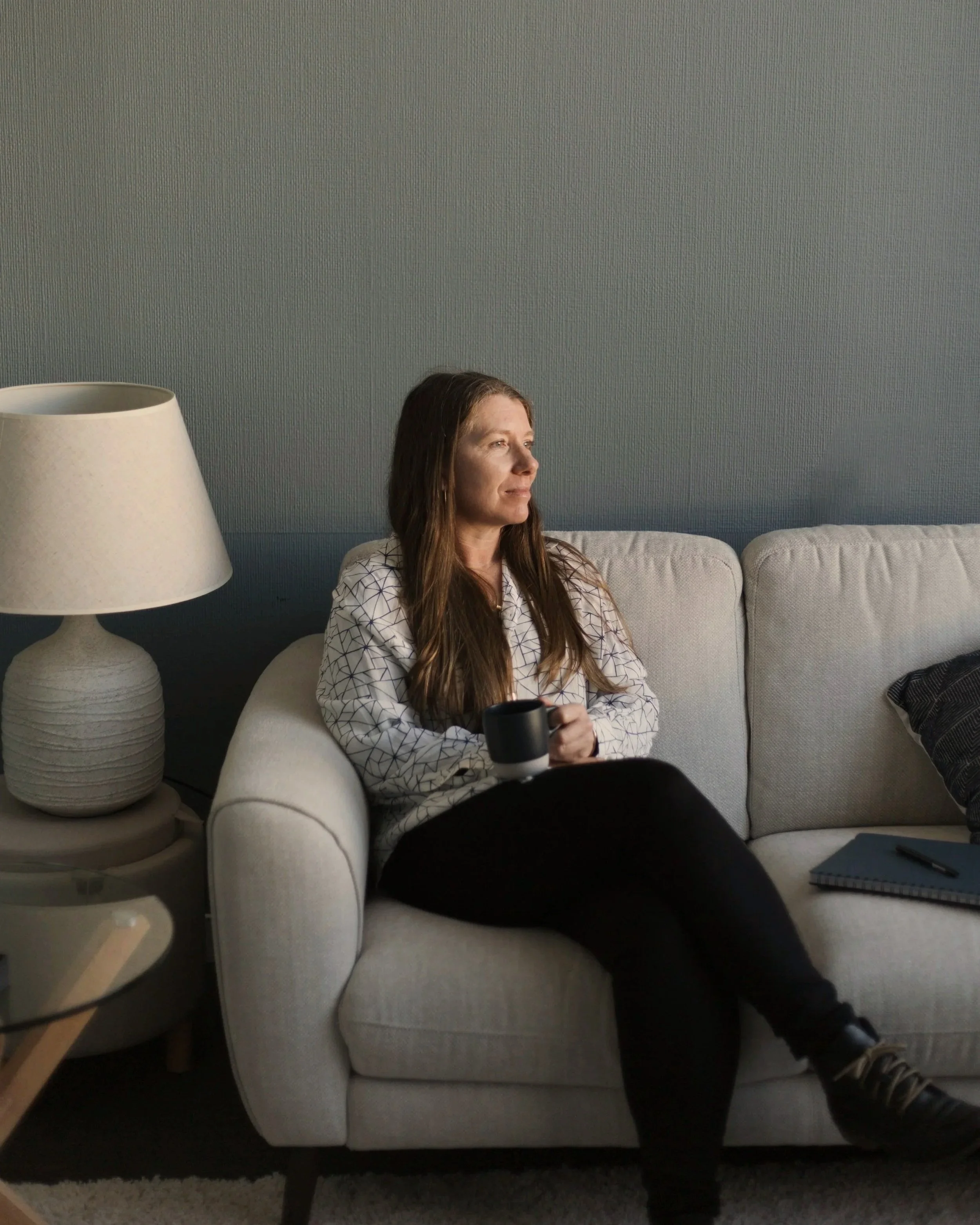 Hayley seated with a cup of tea, looking through a window in a quiet reflective moment