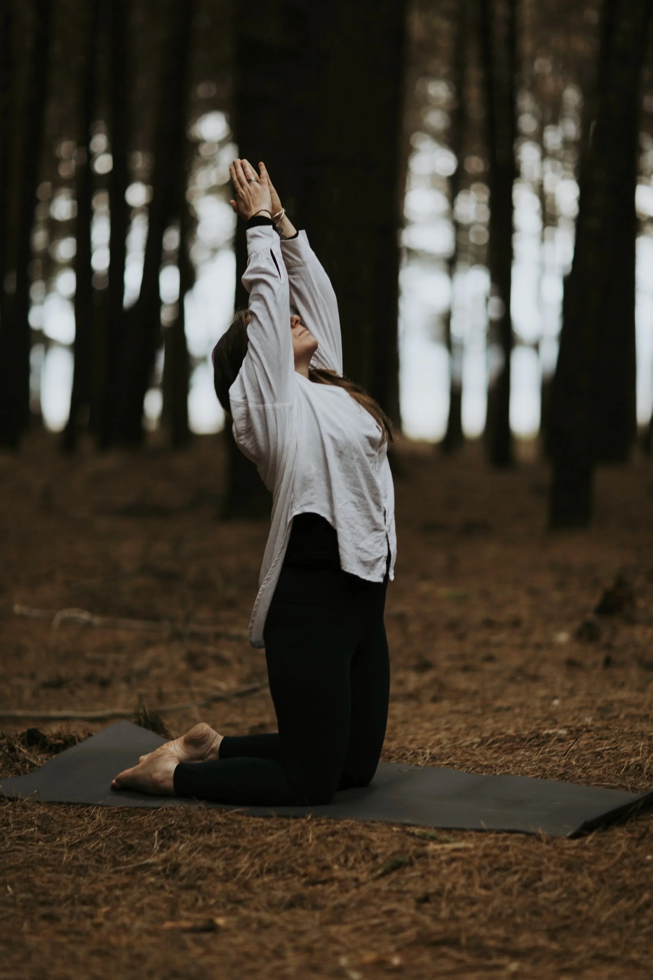 Yoga therapist Hayley standing in the forest with hands raised, expressing openness and embodied movement