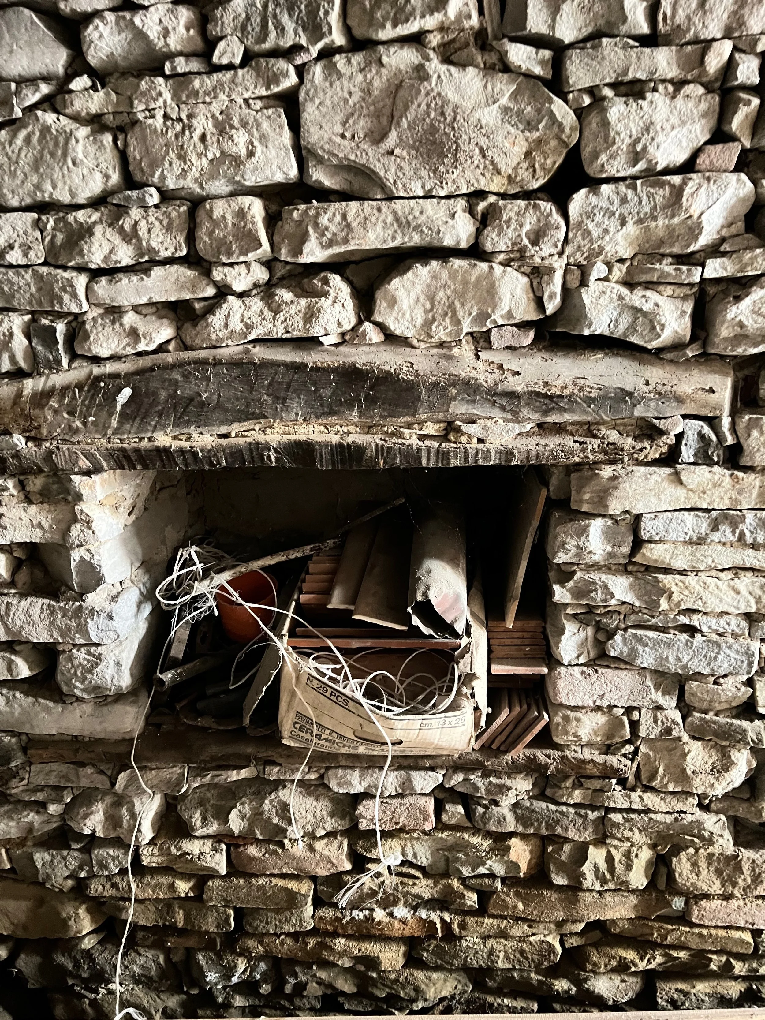 A rustic stone wall with a small opening containing various construction or wiring supplies, including cardboard boxes, wires, bricks, and tools.