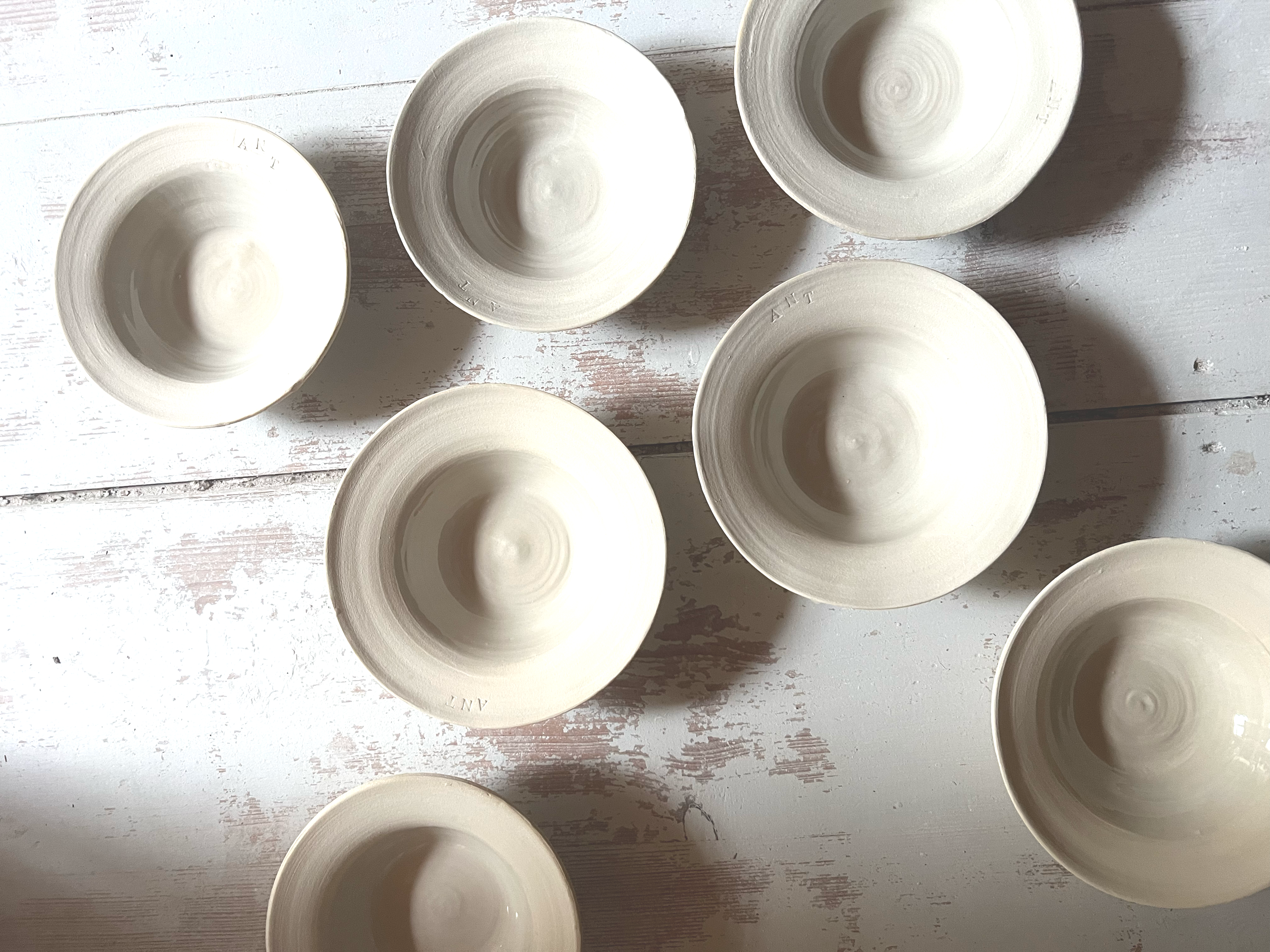 Several cream-colored ceramic bowls arranged on a distressed white wooden surface.