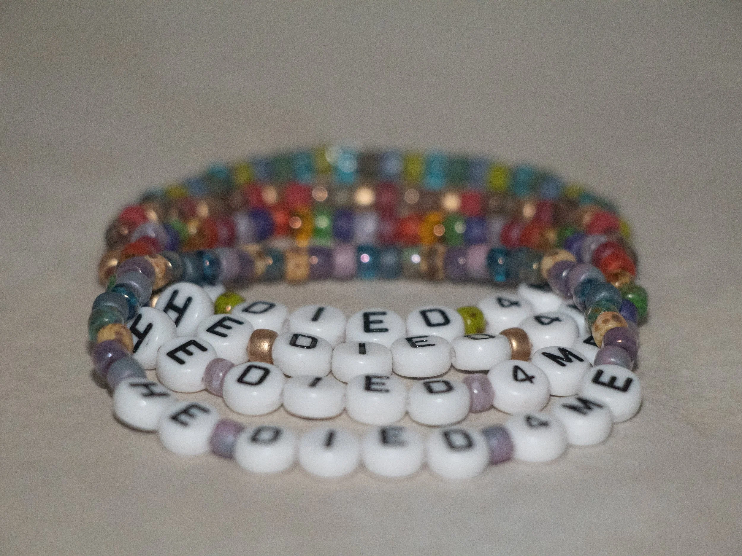 HE DIED 4ME handmade faith bracelets on display in four colorways with seed rocaille beads and white letter beads on stretch elastic.