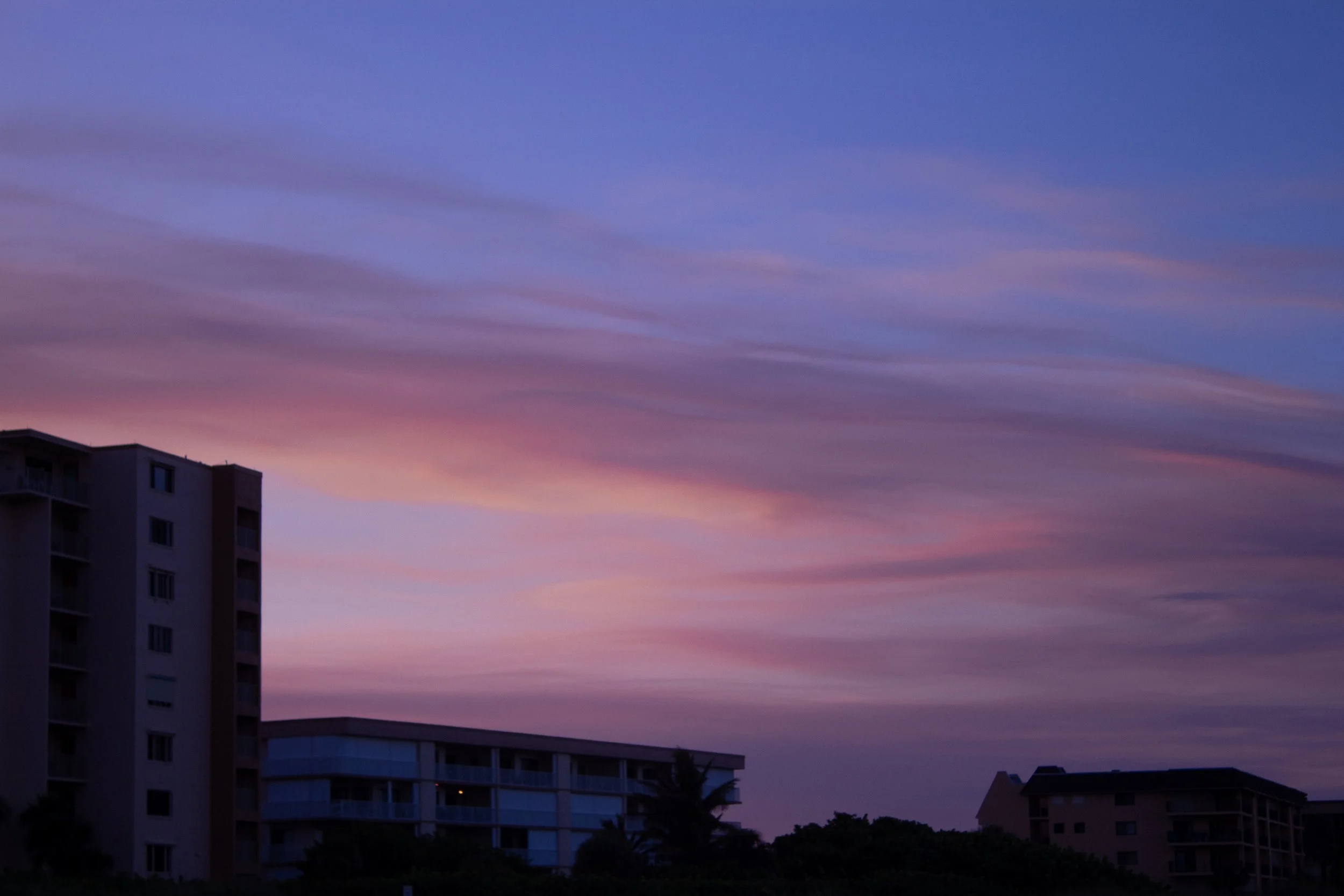 Colorful twilight sky with pink, purple, and blue clouds above silhouettes of buildings.