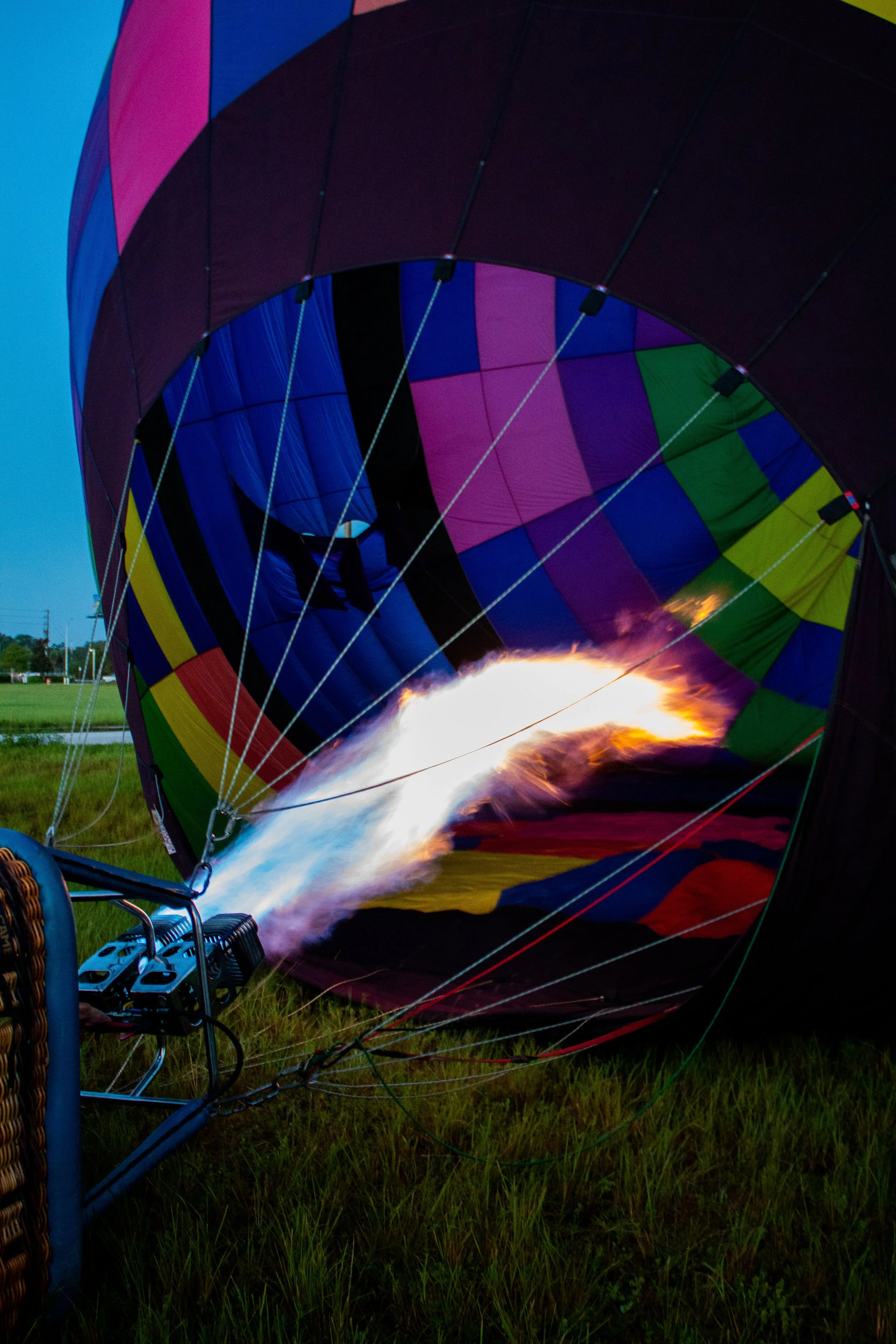 A hot air balloon is being inflated with a flame from the burner, orange and bright yellow in color, with a multicolored patchwork pattern.