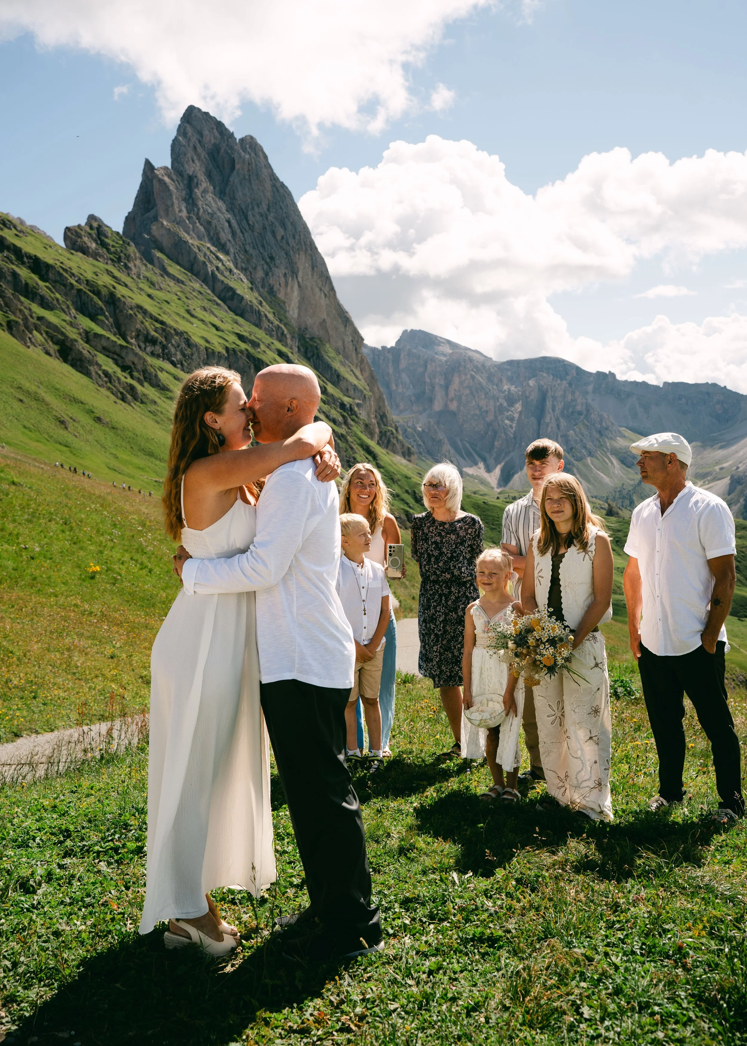 intimate wedding ceremony in the dolomites: bride and groom embracing at Seceda ridge surrounded by their family and children.