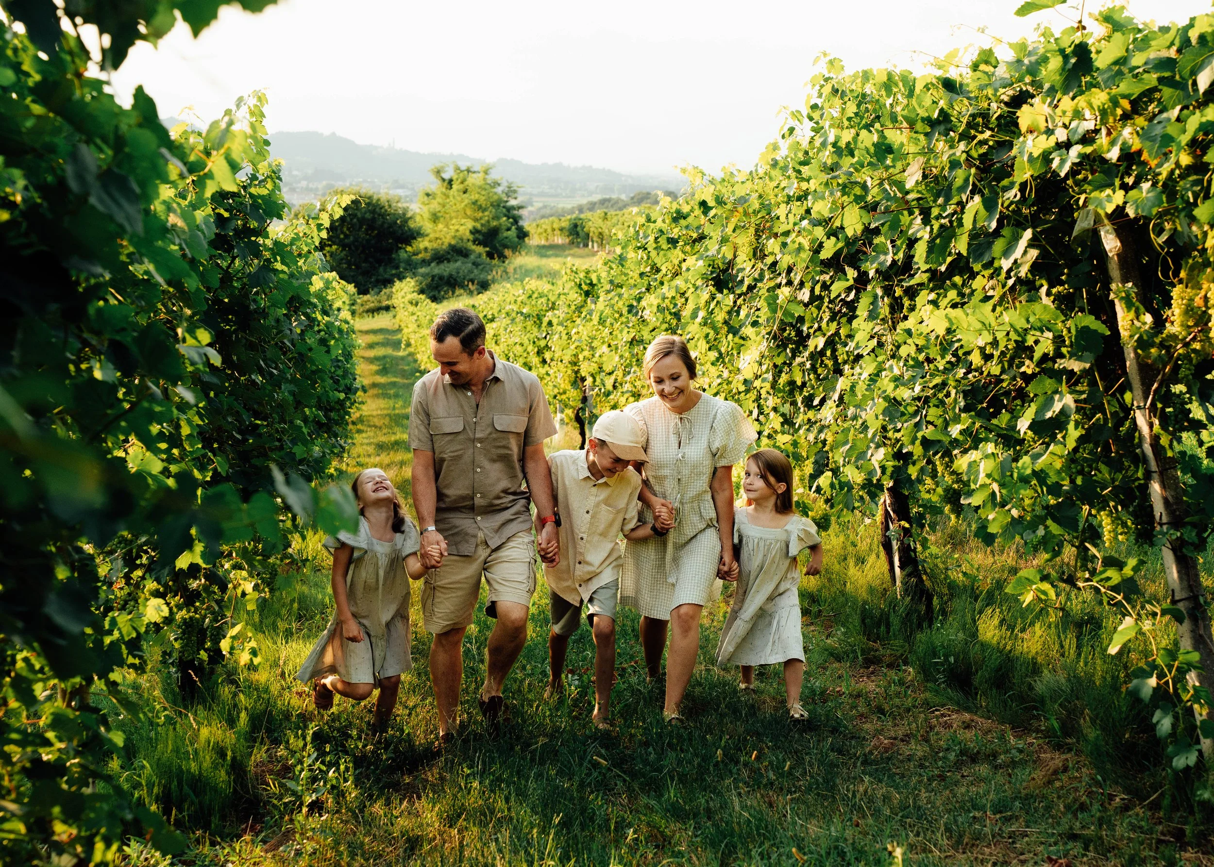 happy family of five walking holding hands through sunlit Italian vineyard during a golden hour family photoshoot.