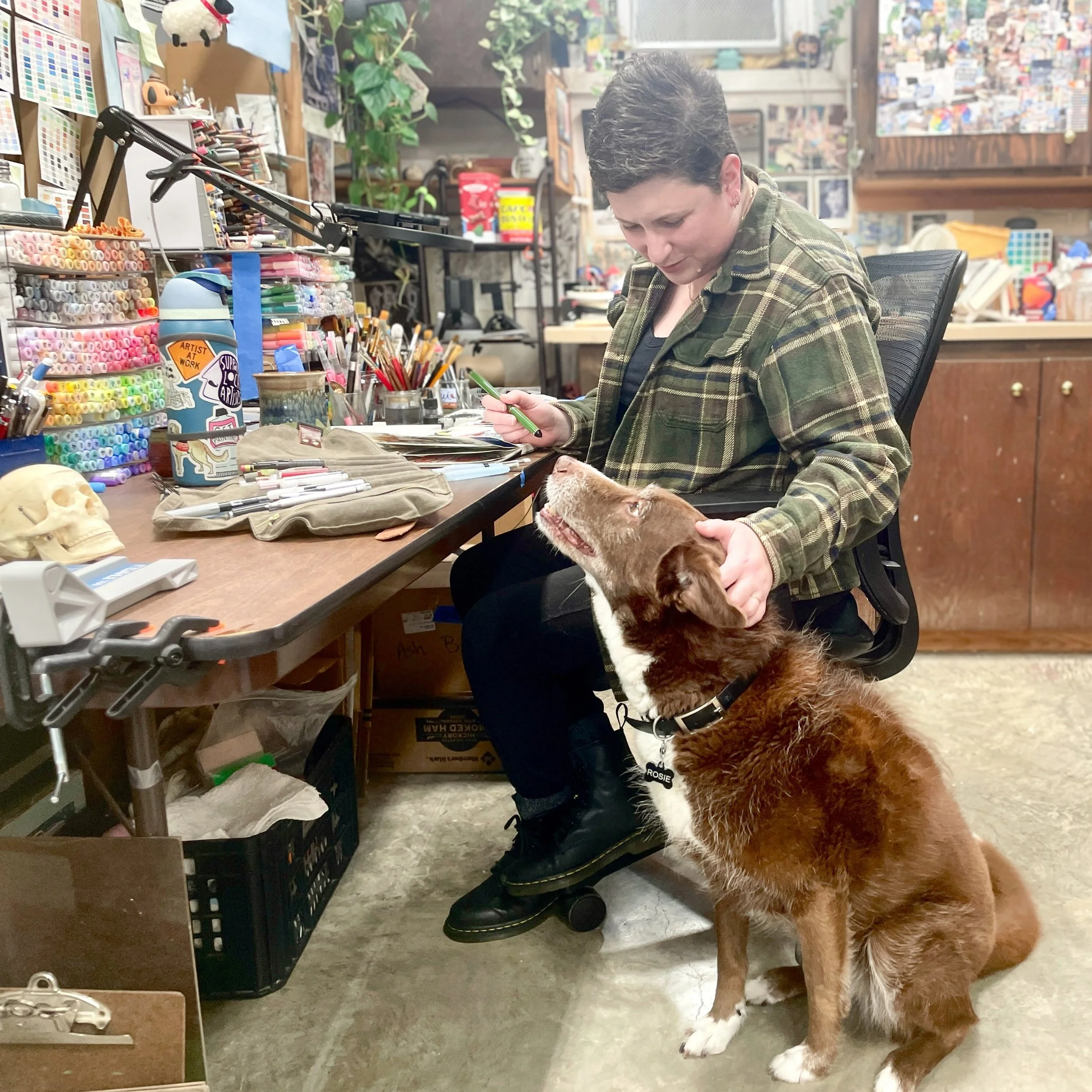 Happy birthday to my studio partner of twelve years. We&rsquo;re graying together, little lady.

accessibility: Ashley sits at her desk, covered in colorful art supplies in her studio, wearing a green flannel, black leggings, and black boots. She loo