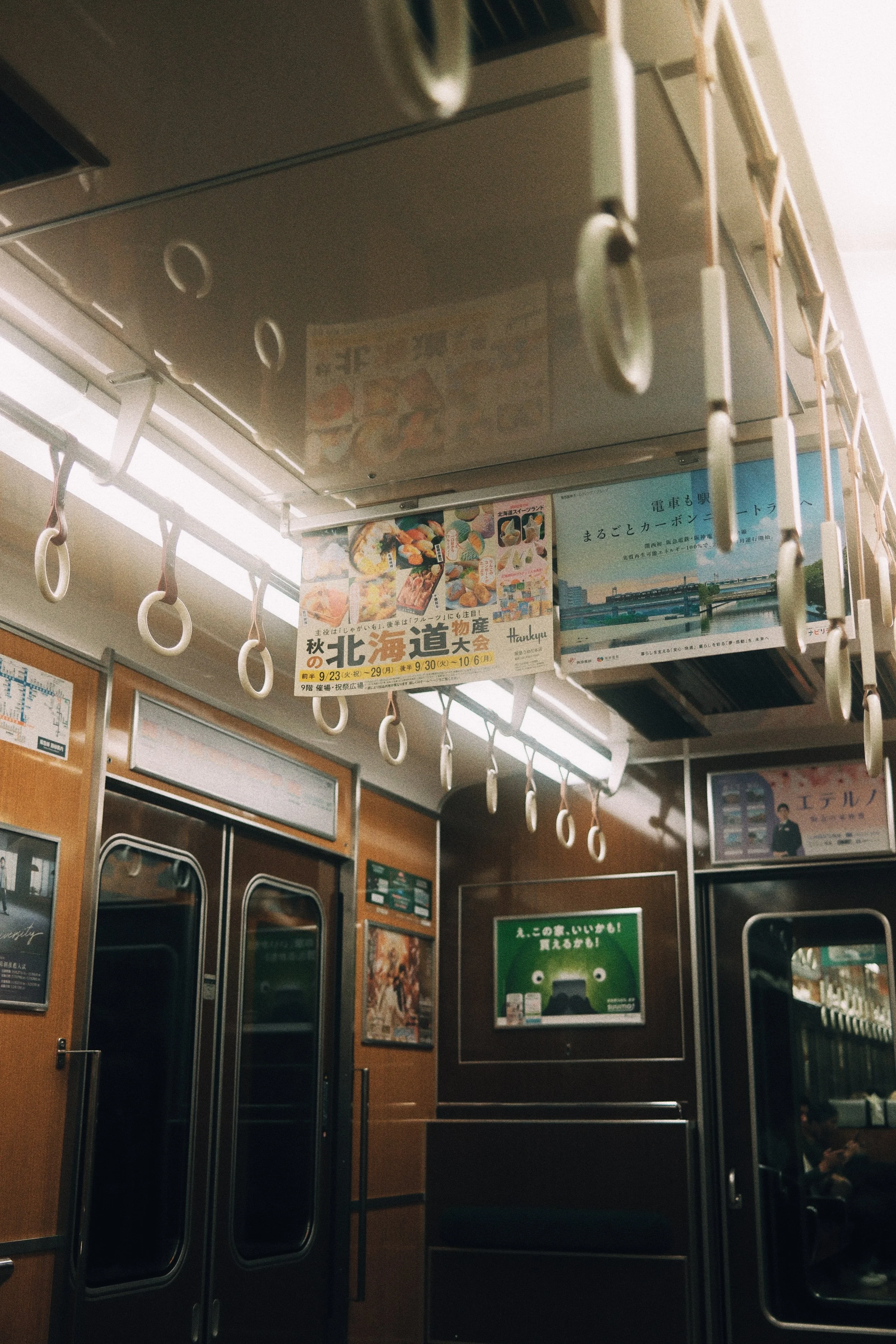 Interior view of a train with hanging hand straps, advertisements, and a closed door.