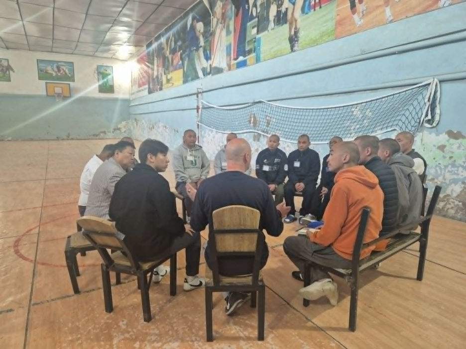 A group of people sitting in a circle in a gymnasium, possibly having a discussion or meeting.