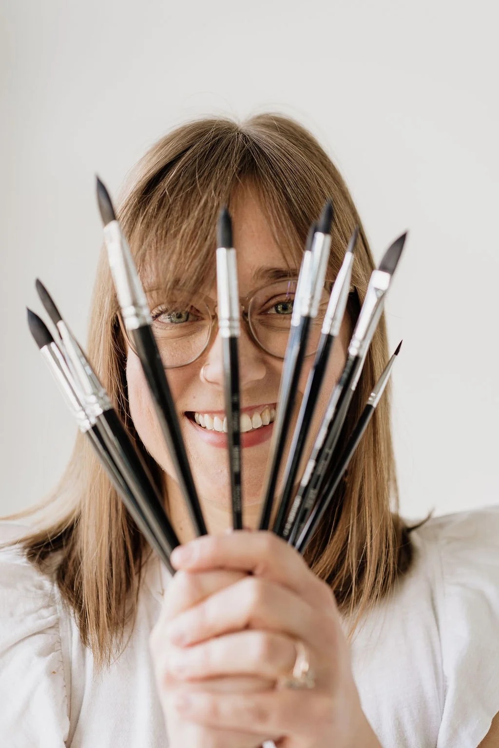 Art therapist in Denver, Leanne Morton, LPC, ATR, holding paintbrushes in front of her face and smiling at the camera.