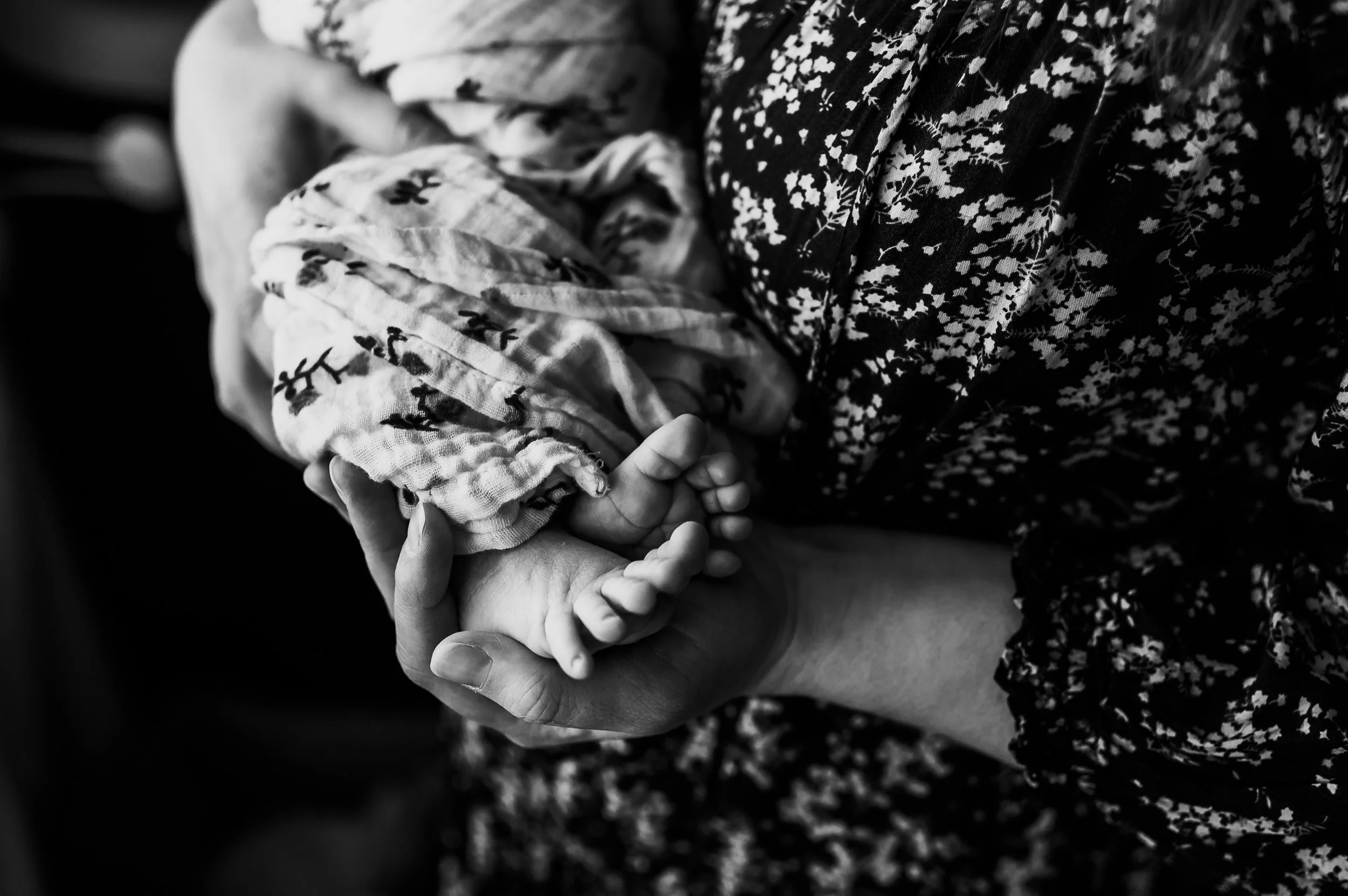 Close-up of a mother's hand holding her baby's tiny foot, postpartum therapy Denver.
