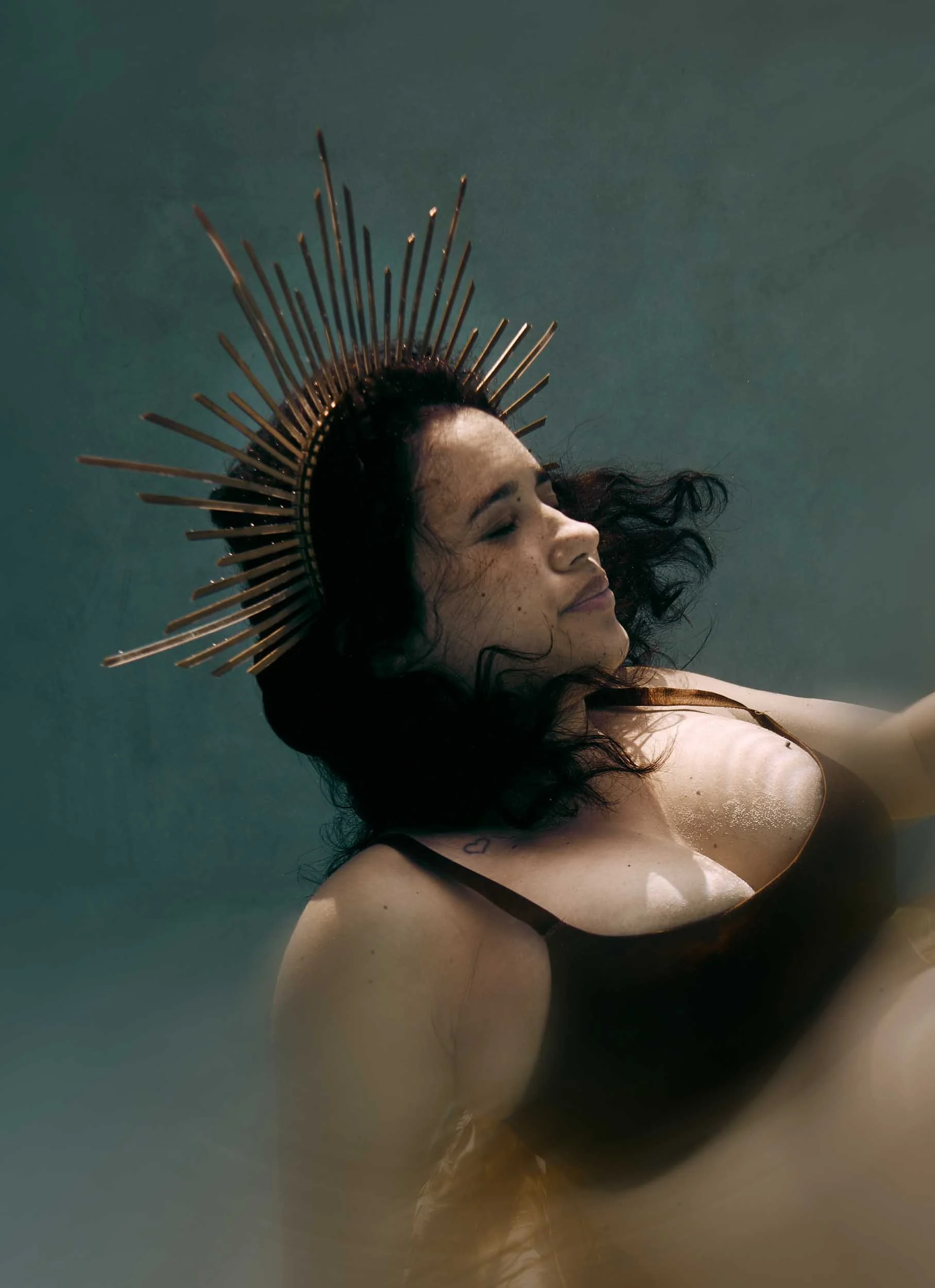 Femme avec couronnes de rayons dorés sur la tête, nageant sous l'eau avec une expression paisible.