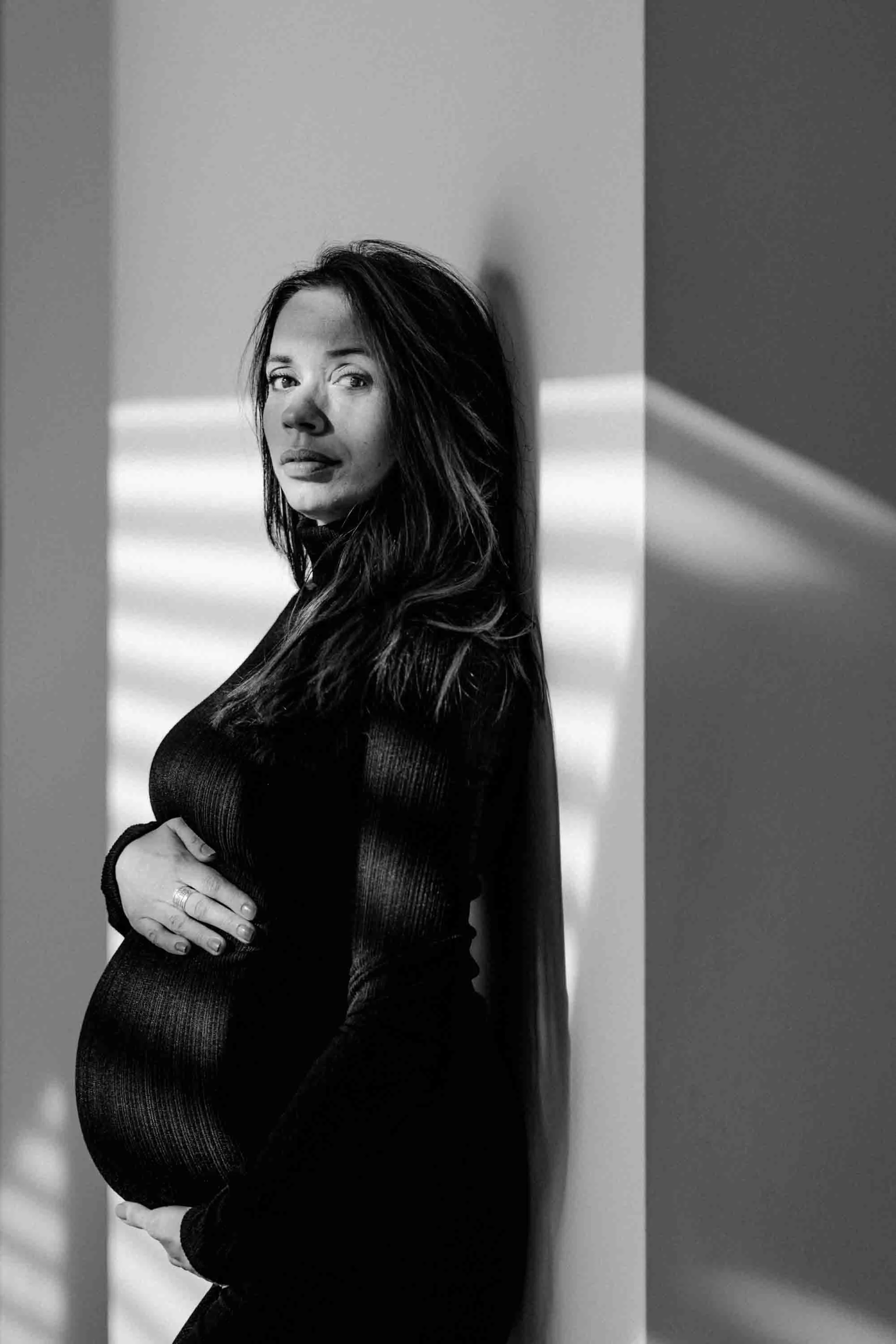 portrait d'une femme enceinte en noir et blanc avec une robe moulante adossée à un mur
