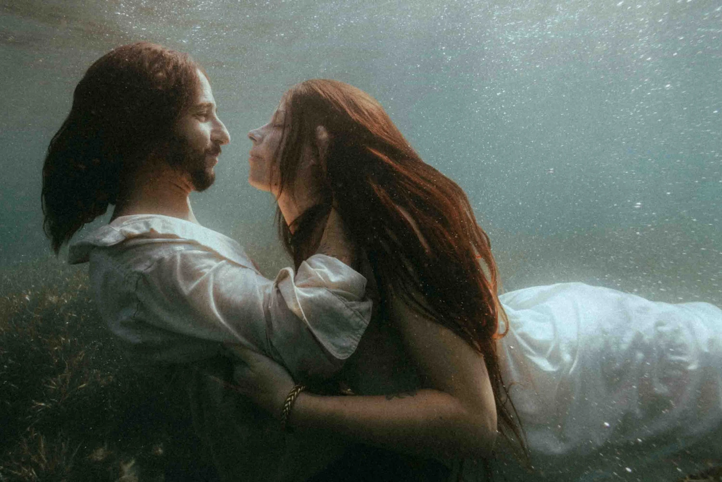 Un homme et une femme nageant sous l'eau, face à face, dans une eau calme.