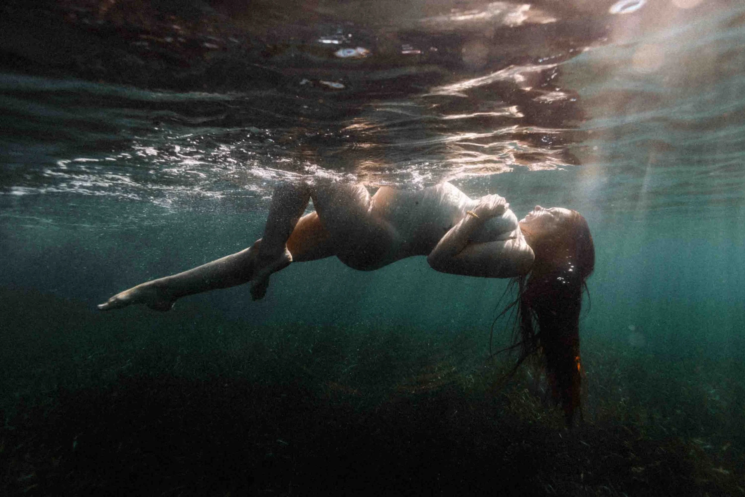une femme nue allongée sur la surface de l'eau, sous l'eau, les cheveux noirs flottants, en position de relaxation